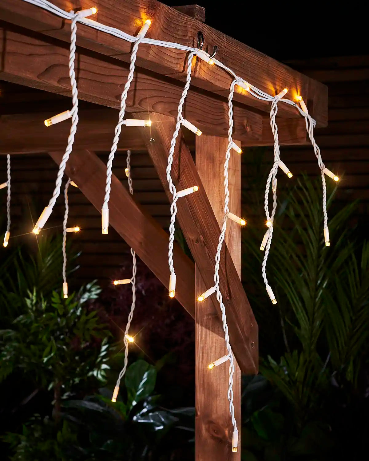 Close-up of warm white twinkling icicle lights with white cable attached to a wooden pergola.