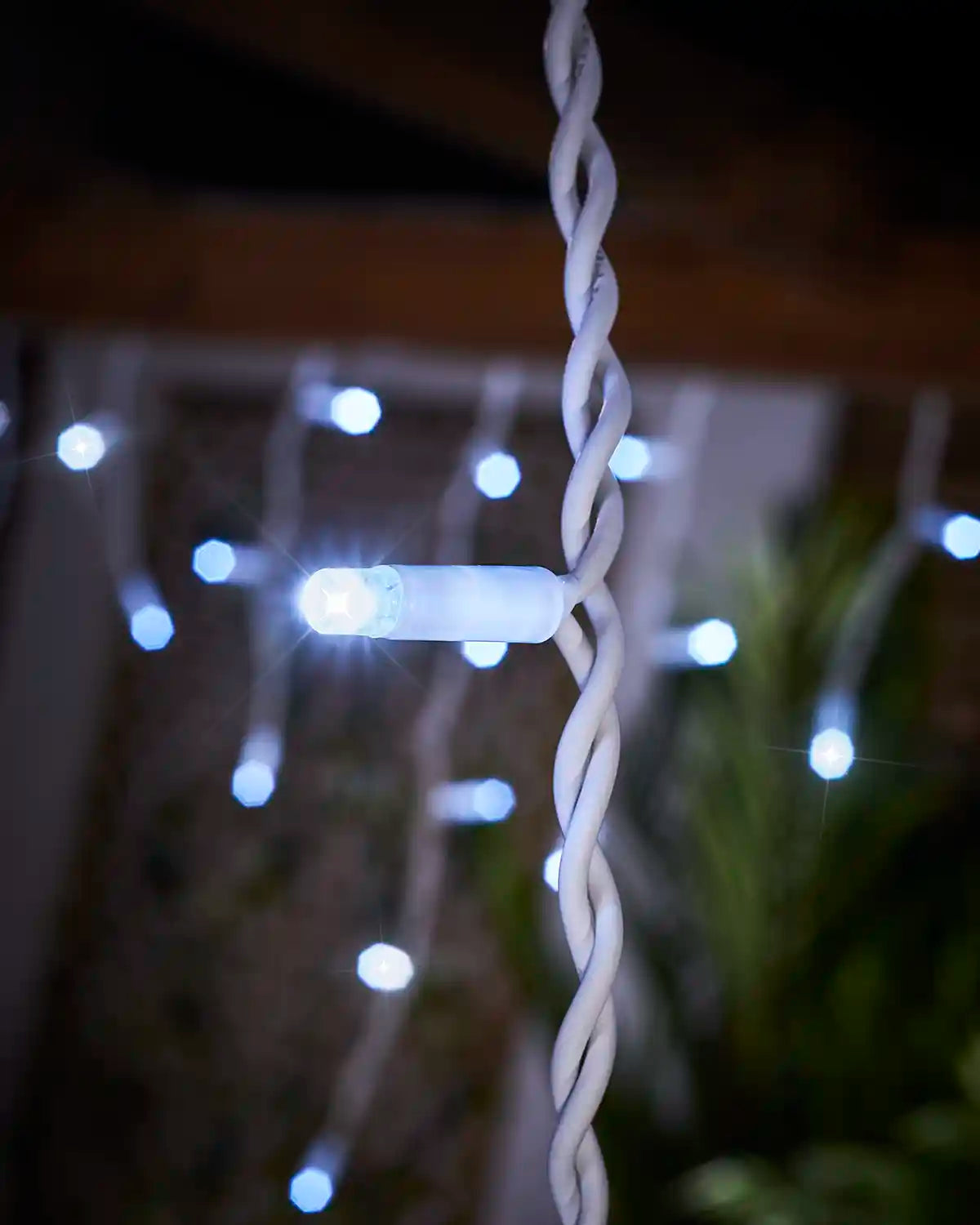 Close-up of a white LED on white twisted cable with blurred icicle lights behind.