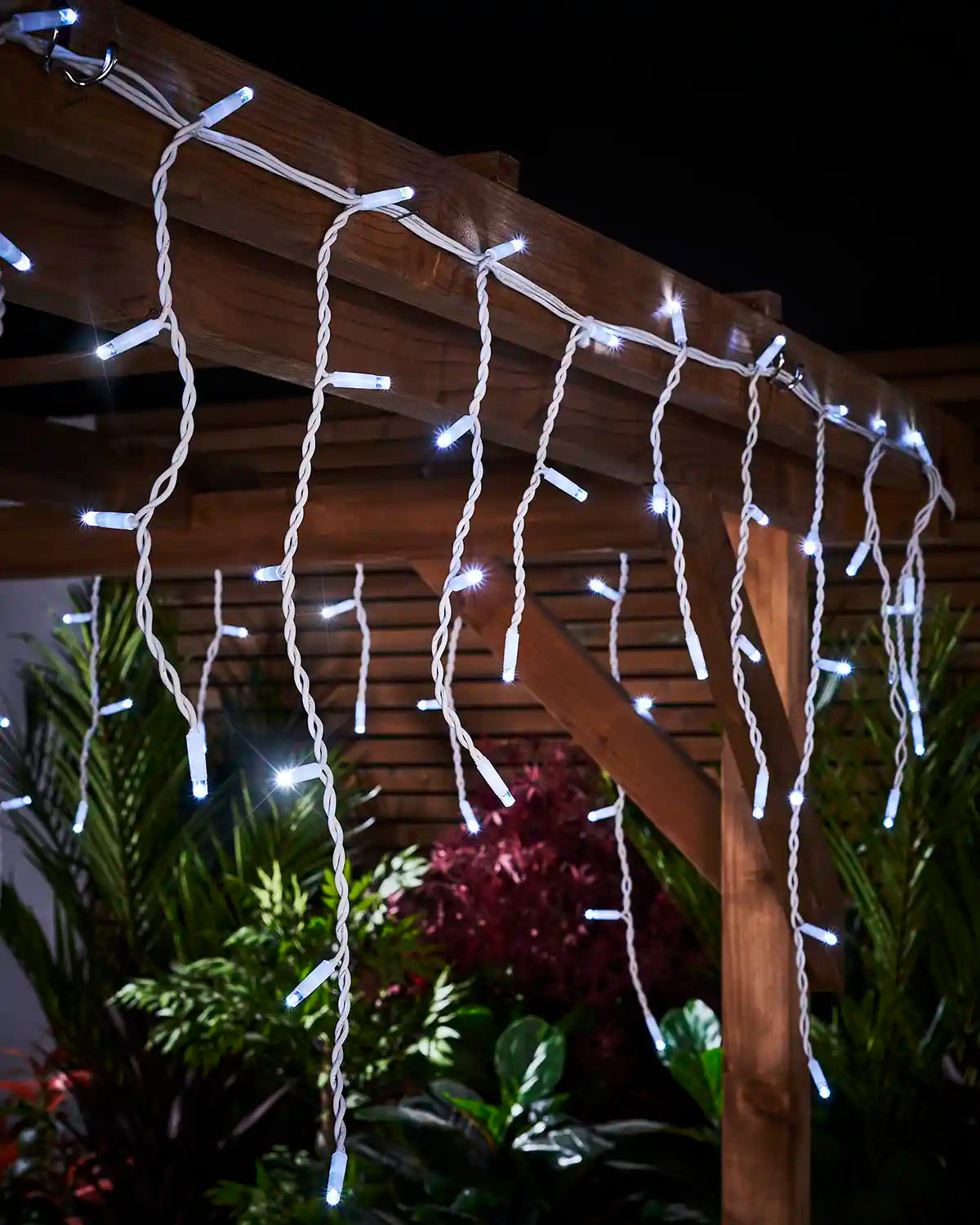 Close-up of white twinkling icicle lights with white cable attached to a wooden pergola.