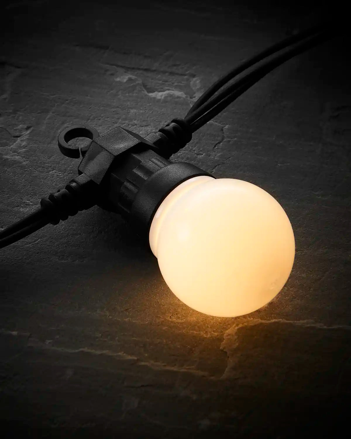 Close-up of a warm white frosted festoon bulb on black cable.