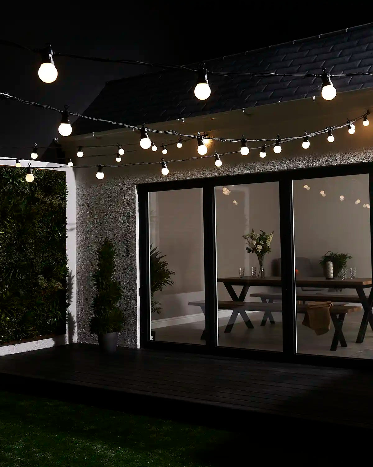 Warm white festoon lights displayed above a garden patio and house exterior.