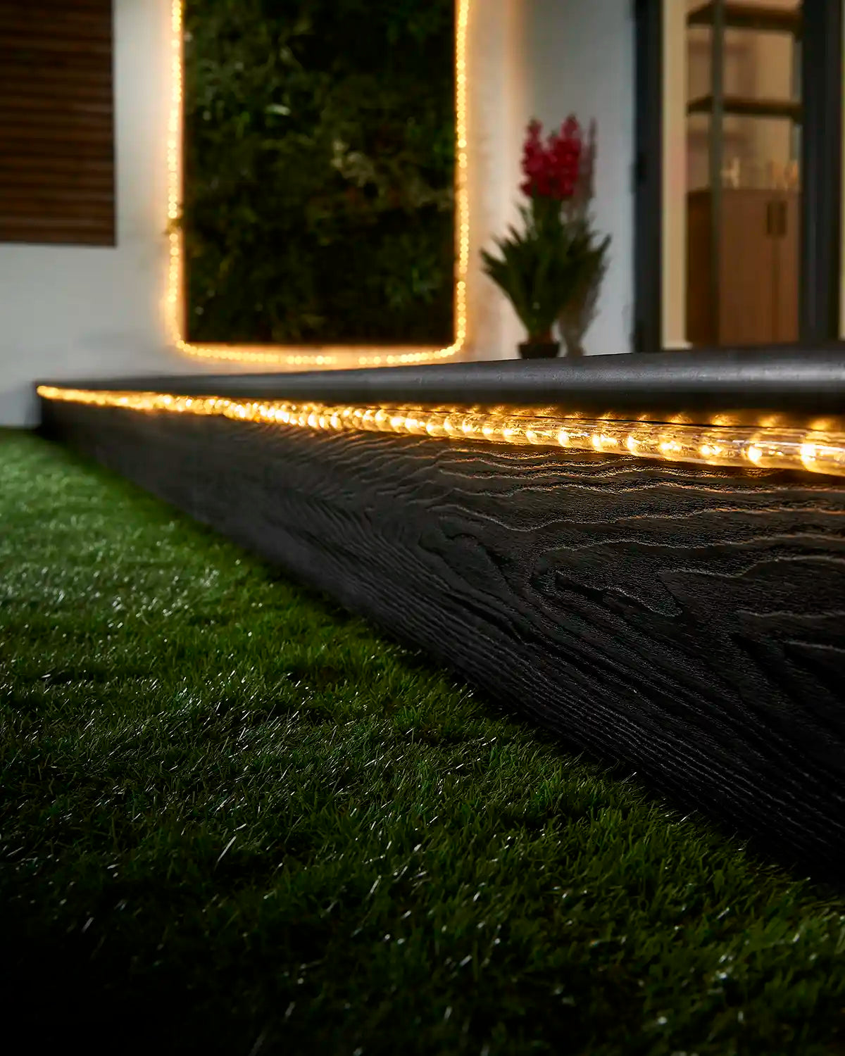 Warm white rope light running along a garden step with a matching lit feature in the background.