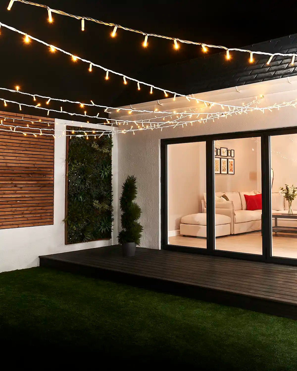 Warm white string lights with white cable suspended overhead across a garden seating area.