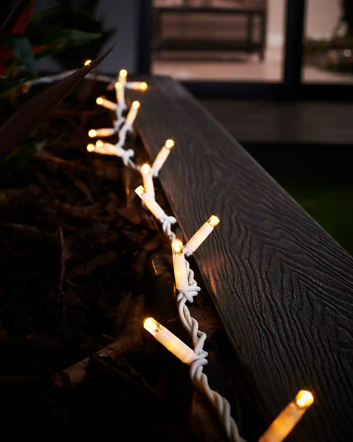 Warm white string lights on a white cable running along an outdoor planter edge.