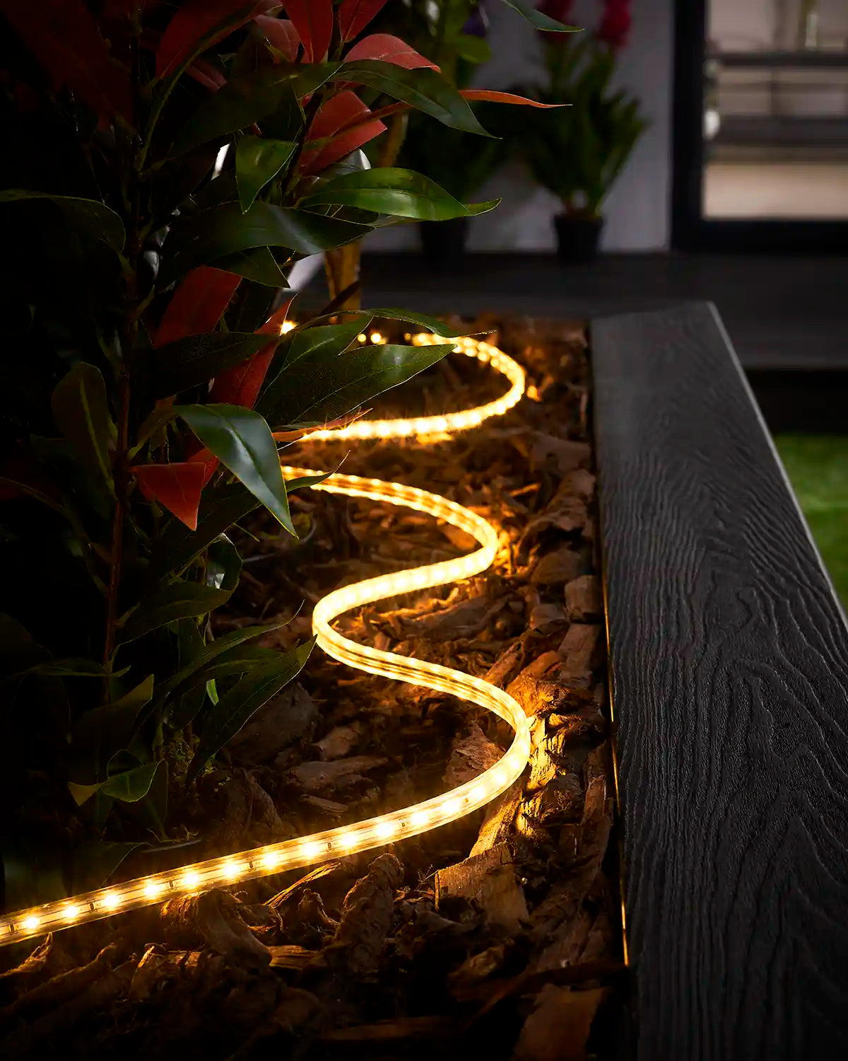 Warm white strip light arranged through bark in a raised garden bed beside outdoor plants.