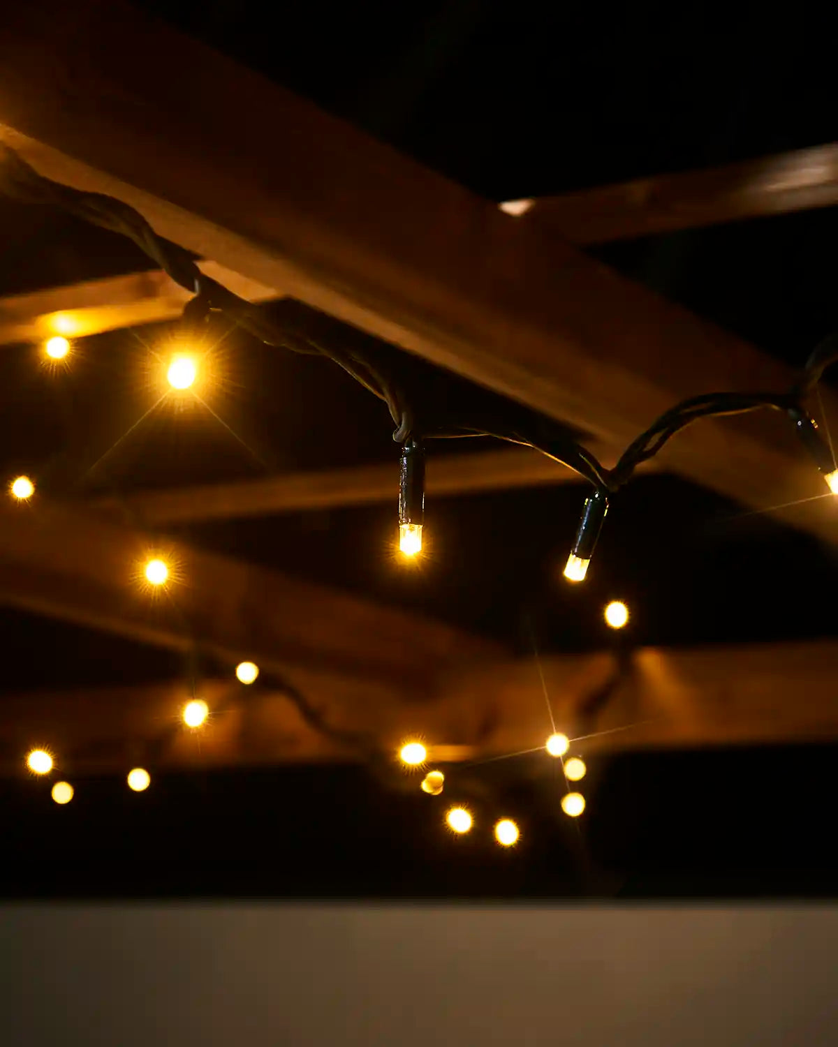 Close-up of warm white twinkle LED string lights hanging from a black cable outdoors.