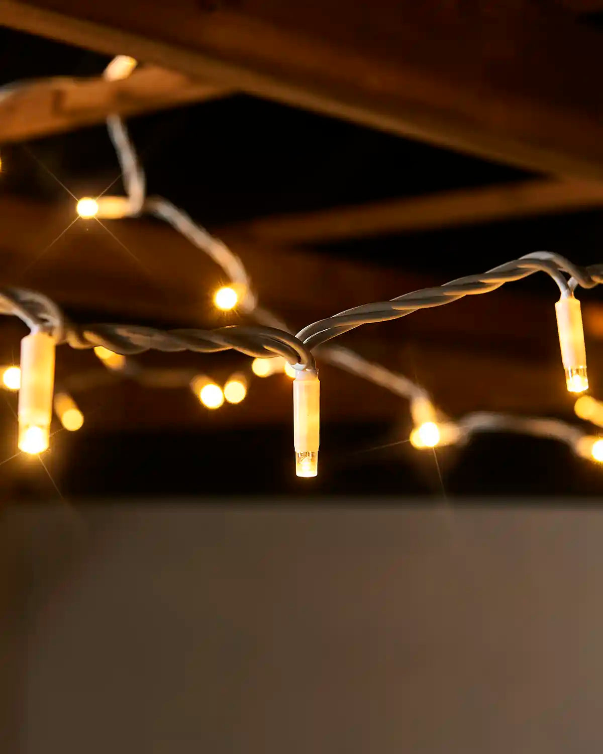 Close-up of warm white twinkle LED string lights hanging from a white cable outdoors.