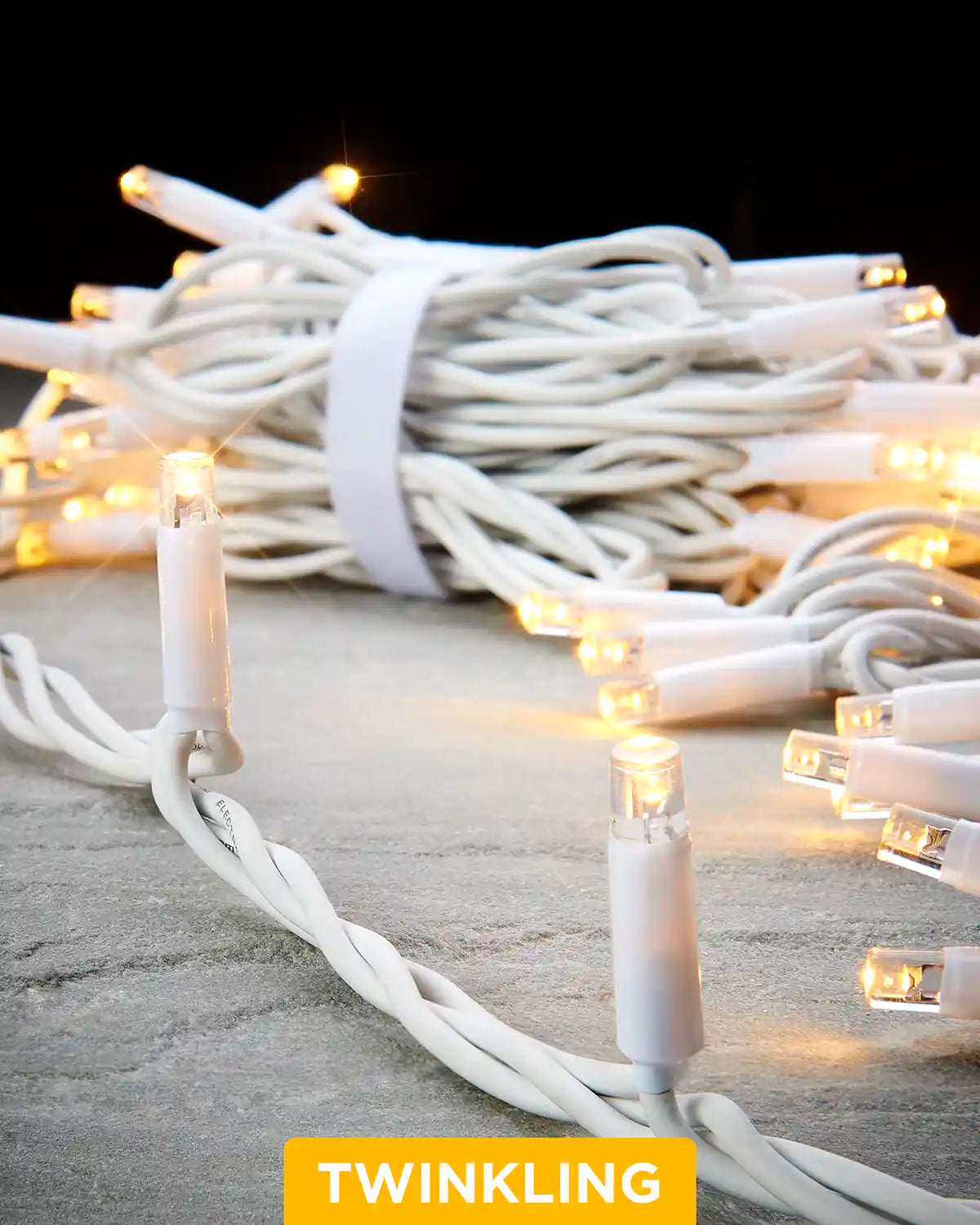 Close-up of warm white Pro Series twinkle string lights with a white cable on a grey surface.