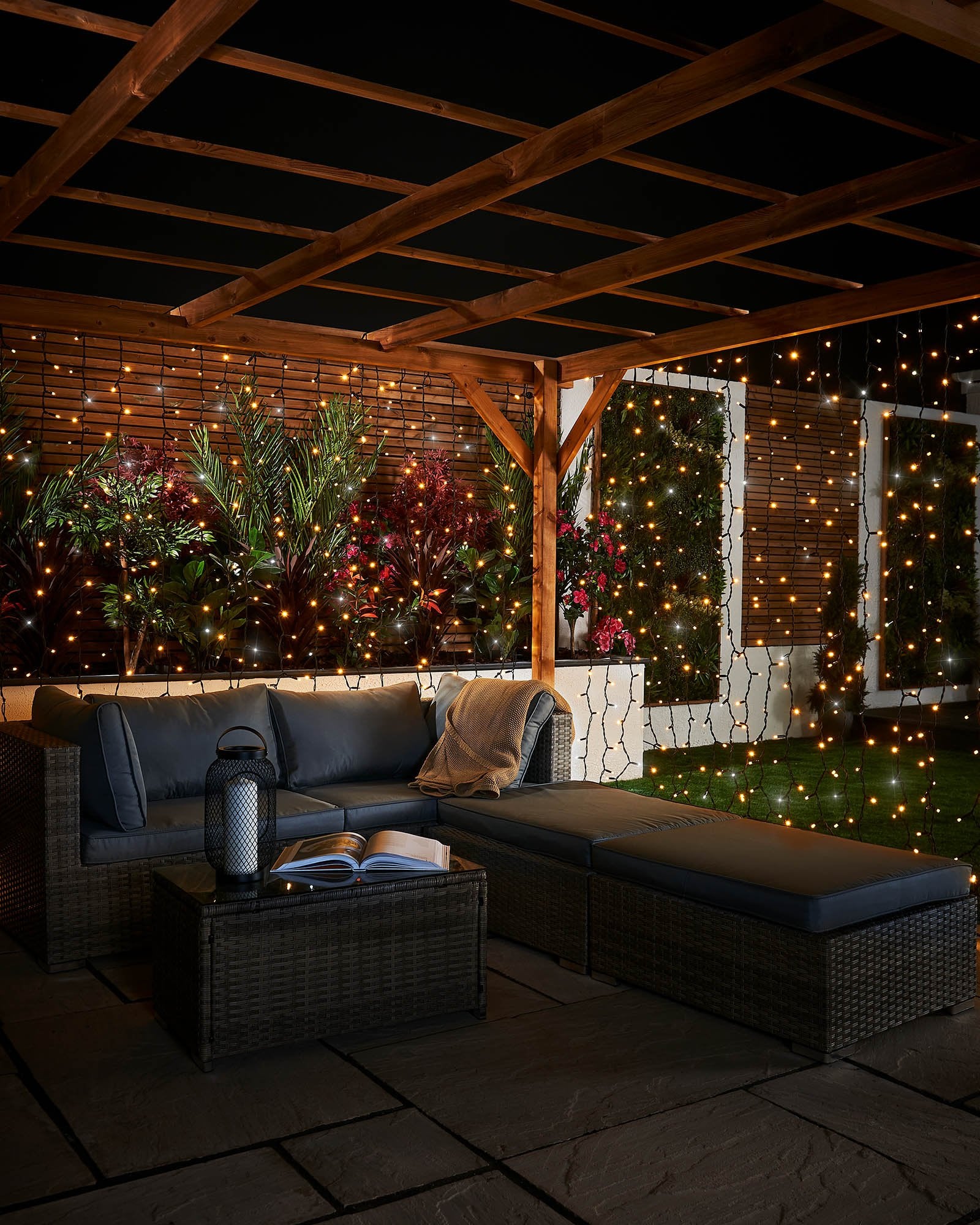 Warm white and white curtain lights with black cable displayed across a covered garden seating area.