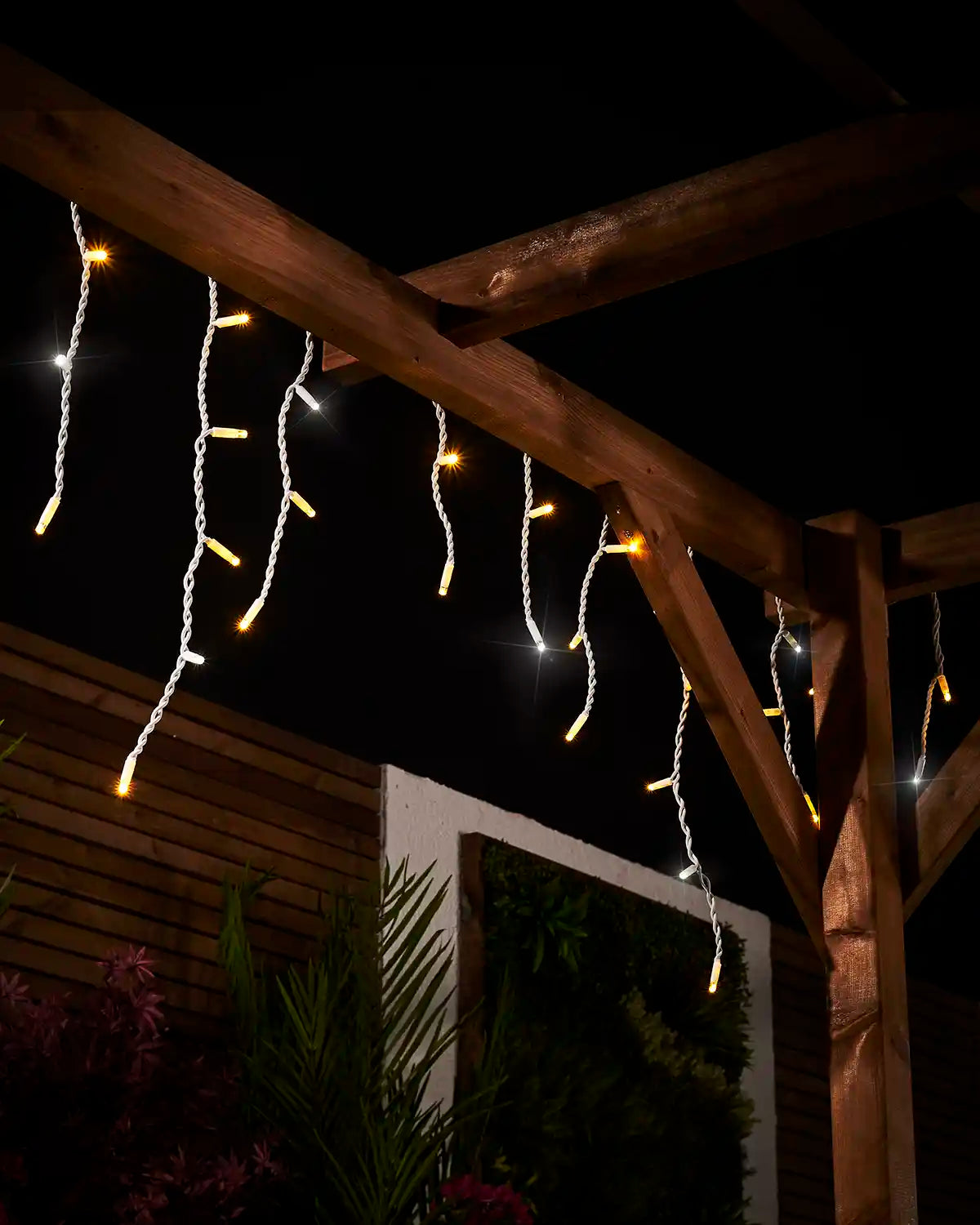 Angled view of warm white and white twinkling icicle lights hanging from a wooden pergola.