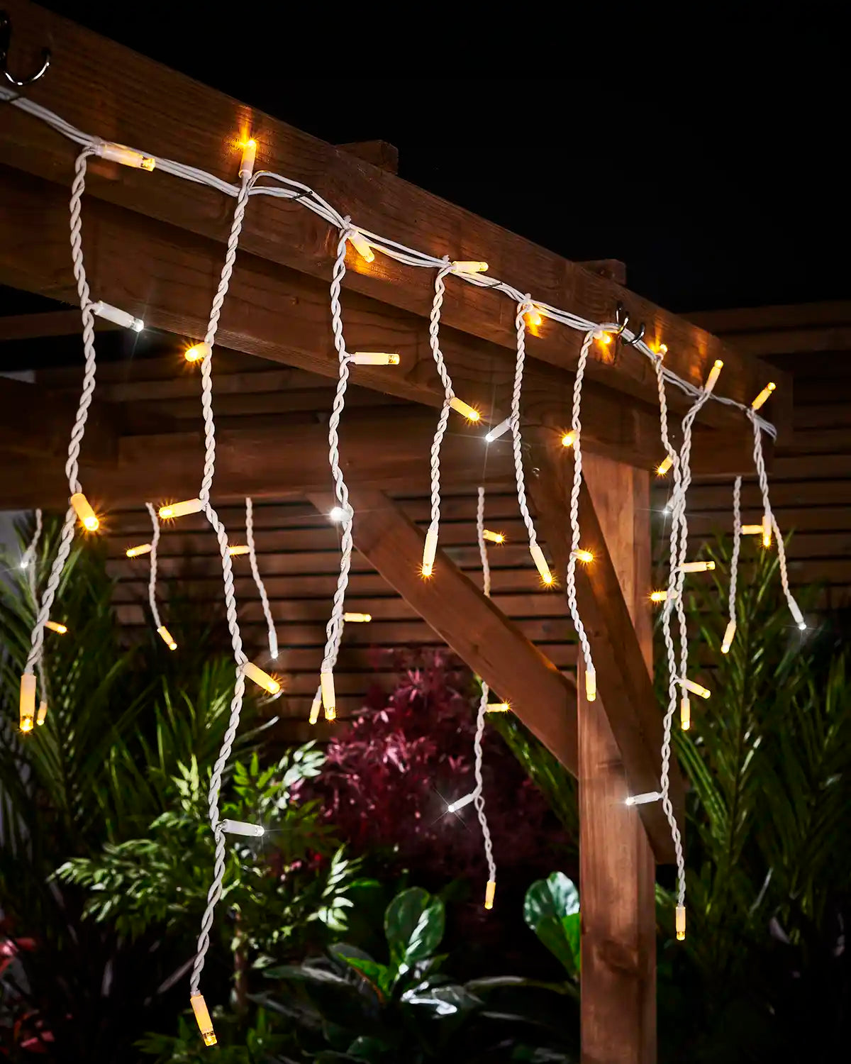 Close-up of warm white and white twinkling icicle lights attached to a wooden pergola beam.