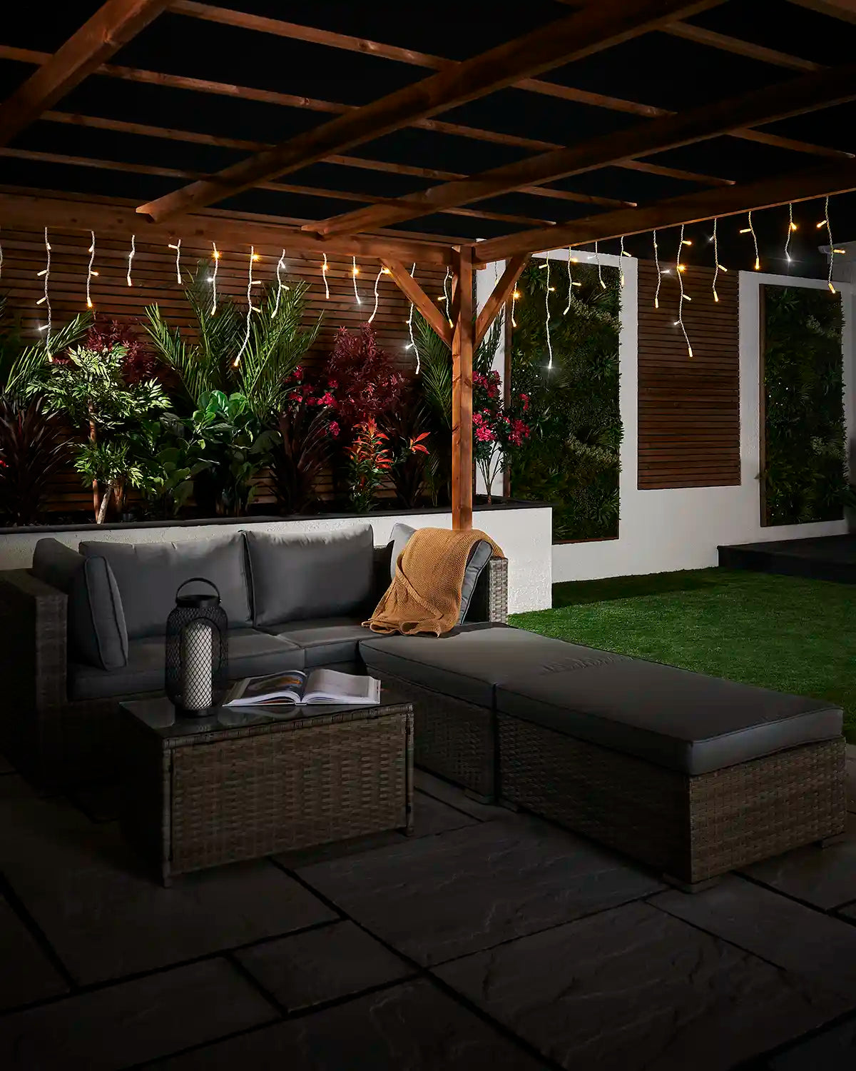 Wide view of warm white and white twinkling icicle lights displayed along a pergola in a garden patio.