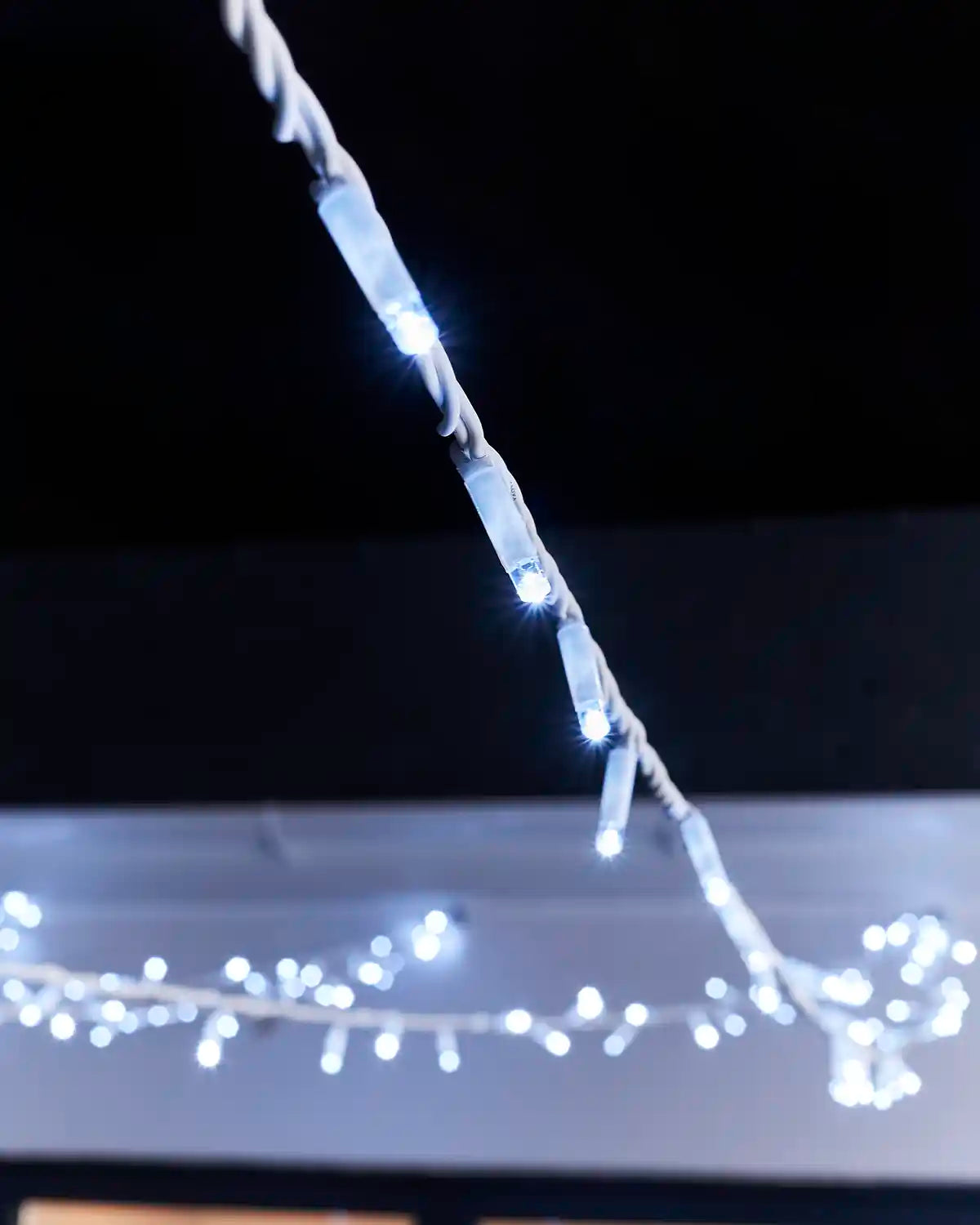 Close-up of white LED string lights on white twisted cable.