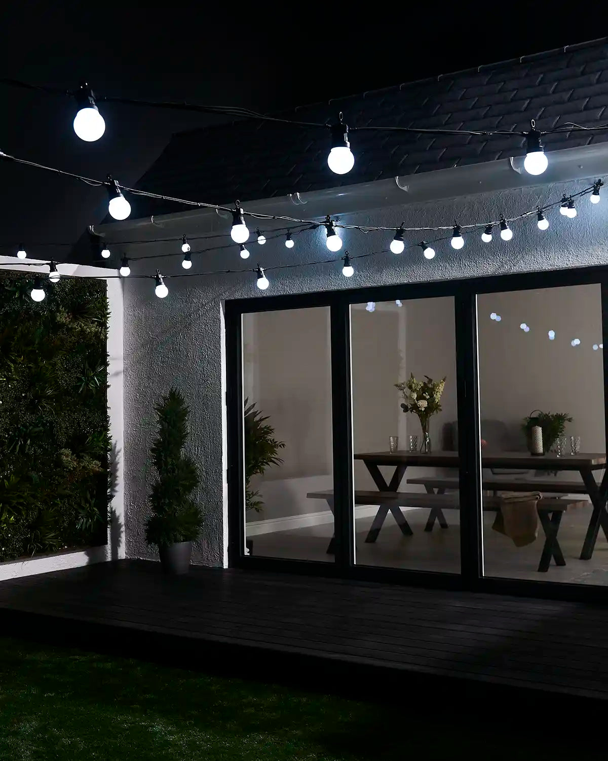 White festoon lights displayed above a garden patio and house exterior.