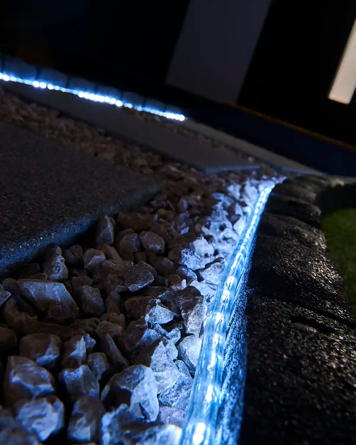 White rope light illuminating a stone border beside outdoor paving and gravel.