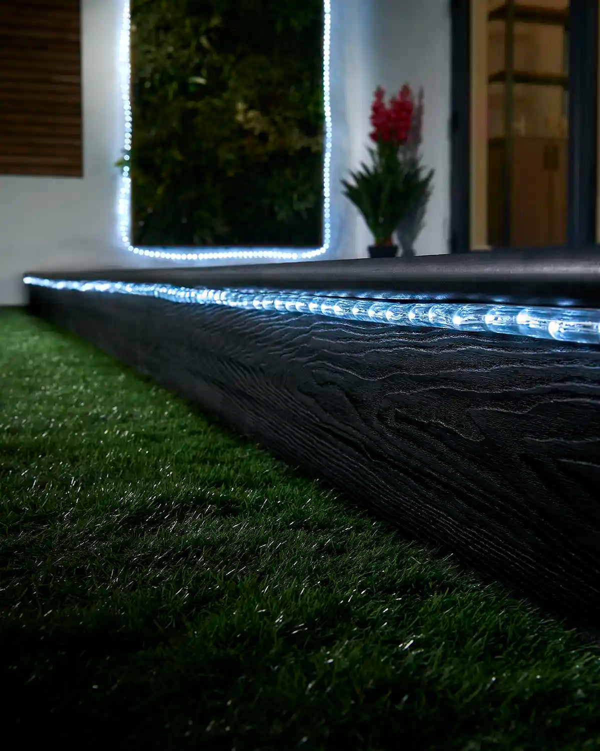 White rope light running along a garden step with a matching lit feature in the background.