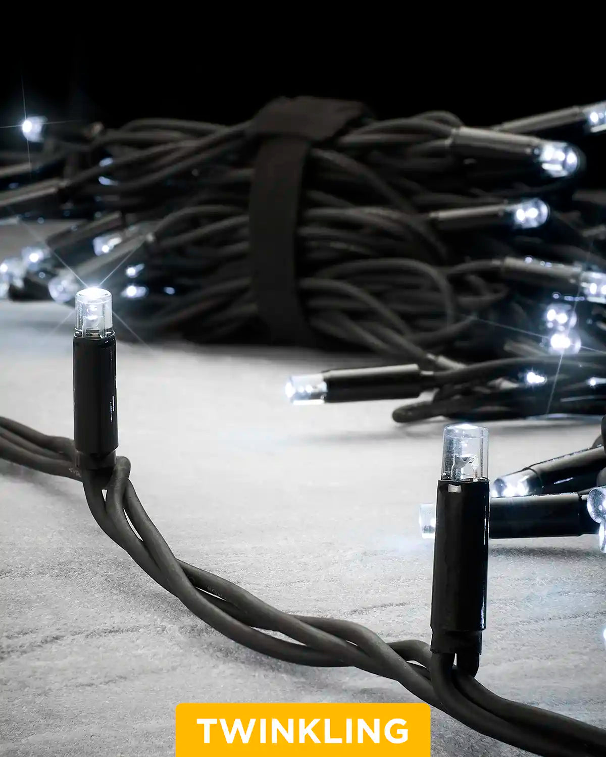 Close-up of white Pro Series twinkle string lights with a black cable on a grey surface.