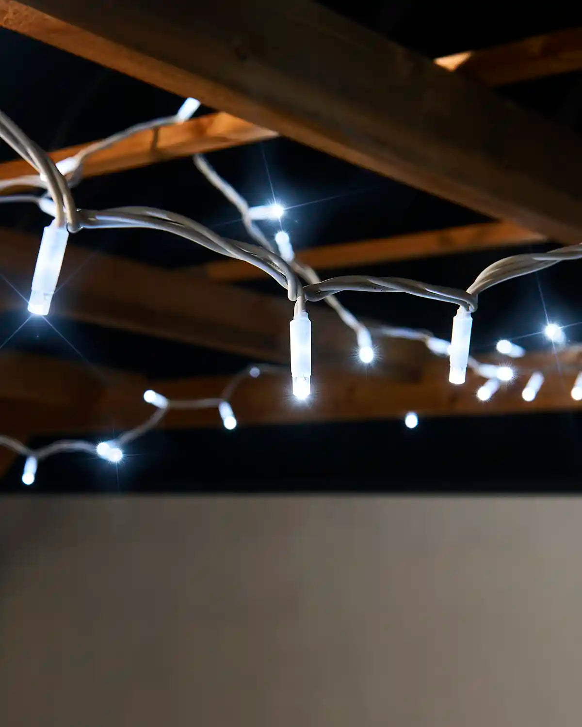 Close-up of white twinkle LED string lights hanging from a white cable outdoors.