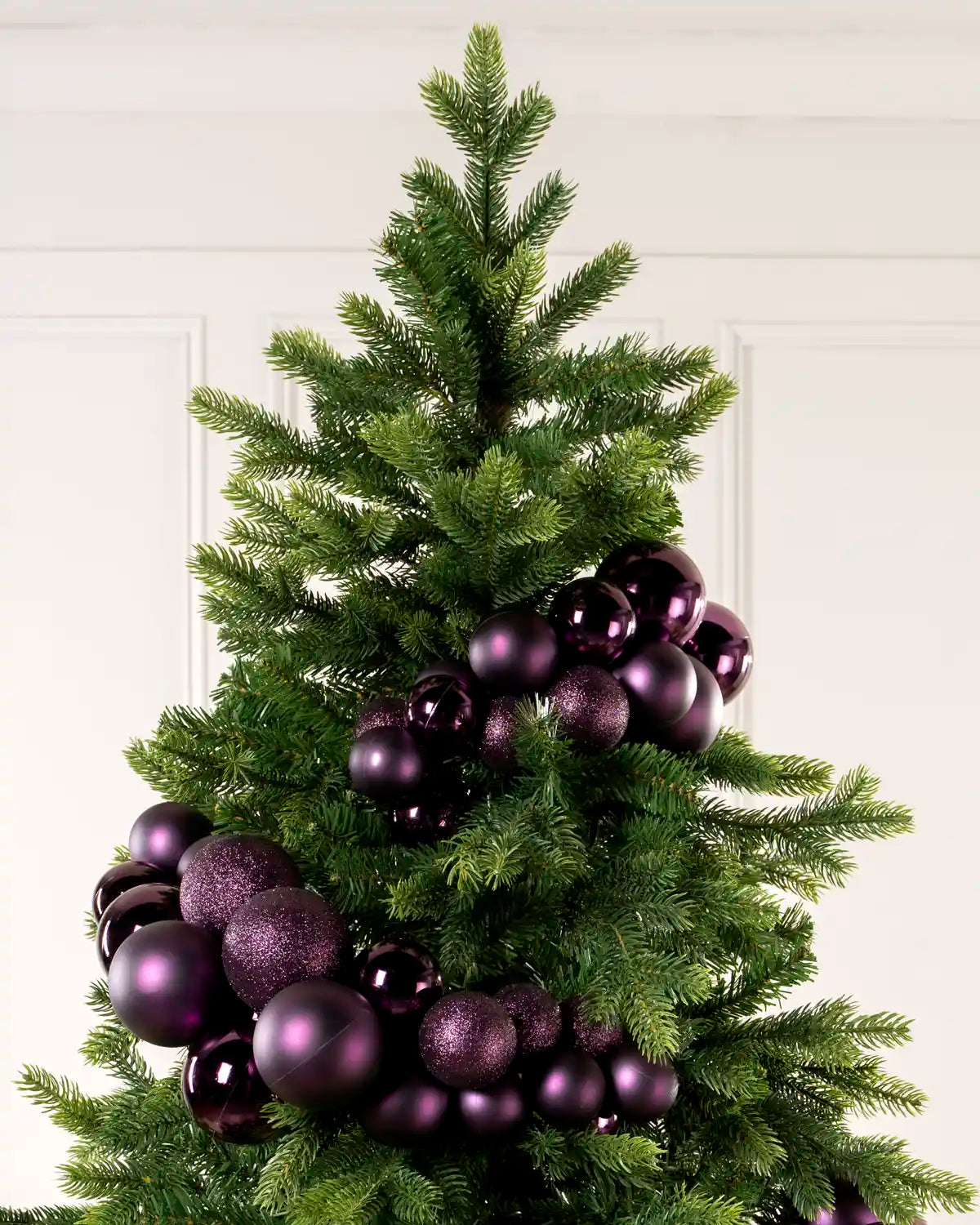 Purple bauble cluster arch arranged through the upper branches of a green Christmas tree.