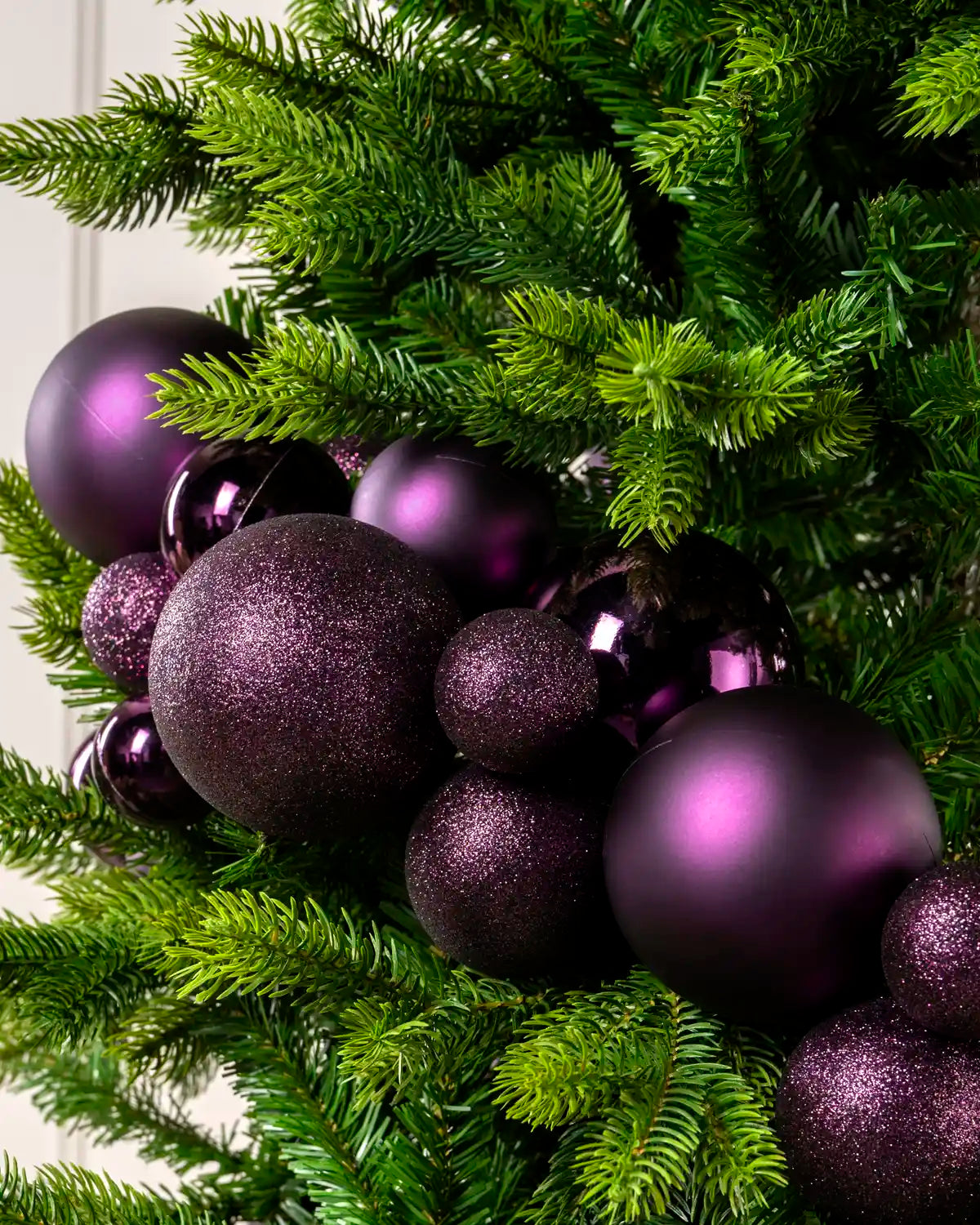 Close-up of purple bauble garland on a Christmas tree showing mixed sizes, matt, shiny and glitter finishes.