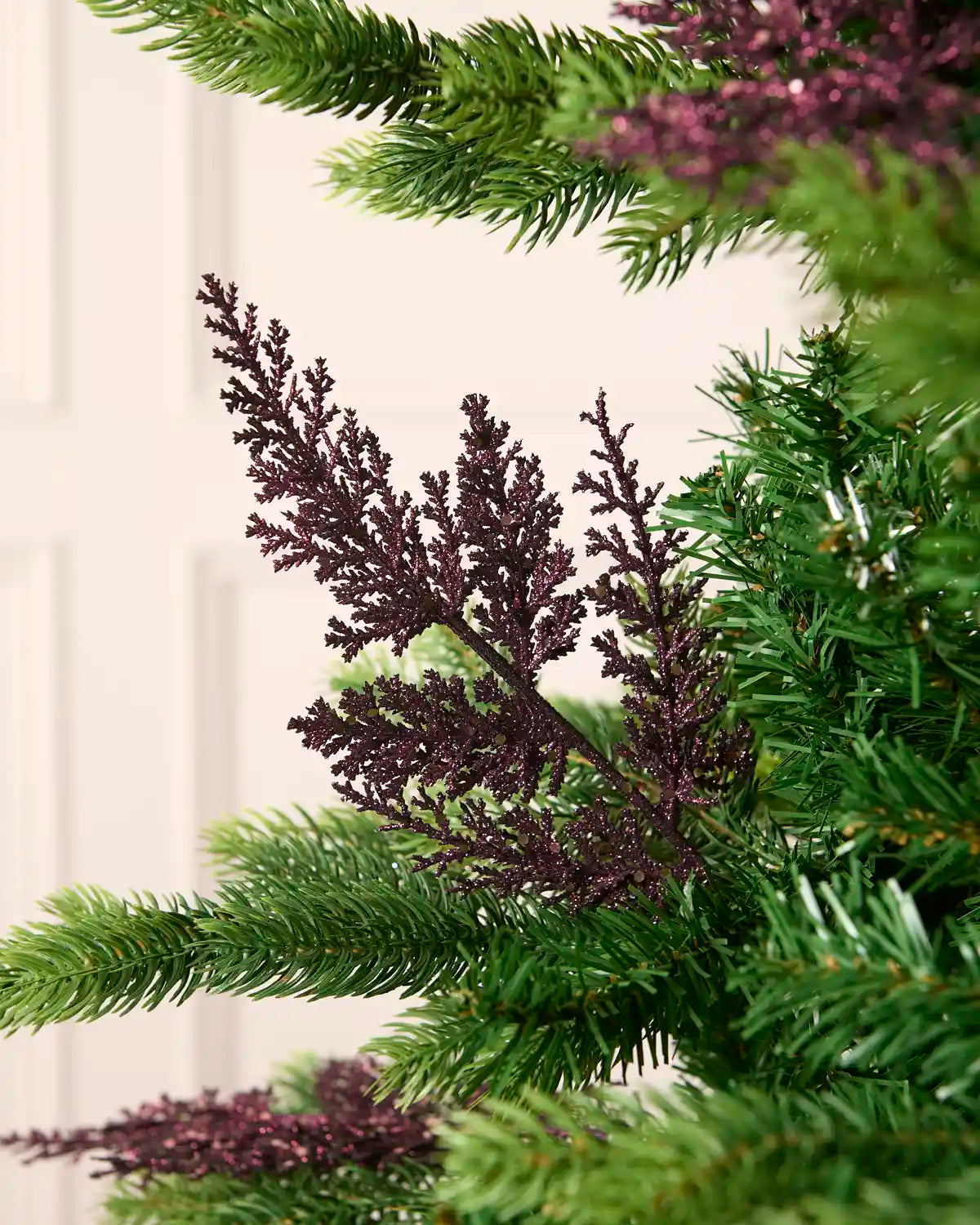 Purple glitter leaf pick arranged amongst green Christmas tree branches.