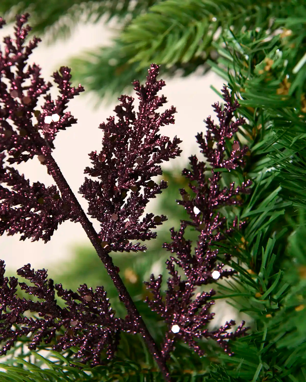 Detailed view of purple glitter foliage with reflective sequins amongst Christmas tree branches.