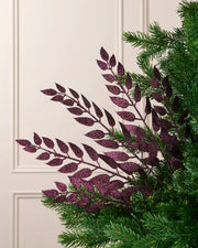 Purple leaf Christmas tree spray arranged among green Christmas tree branches.