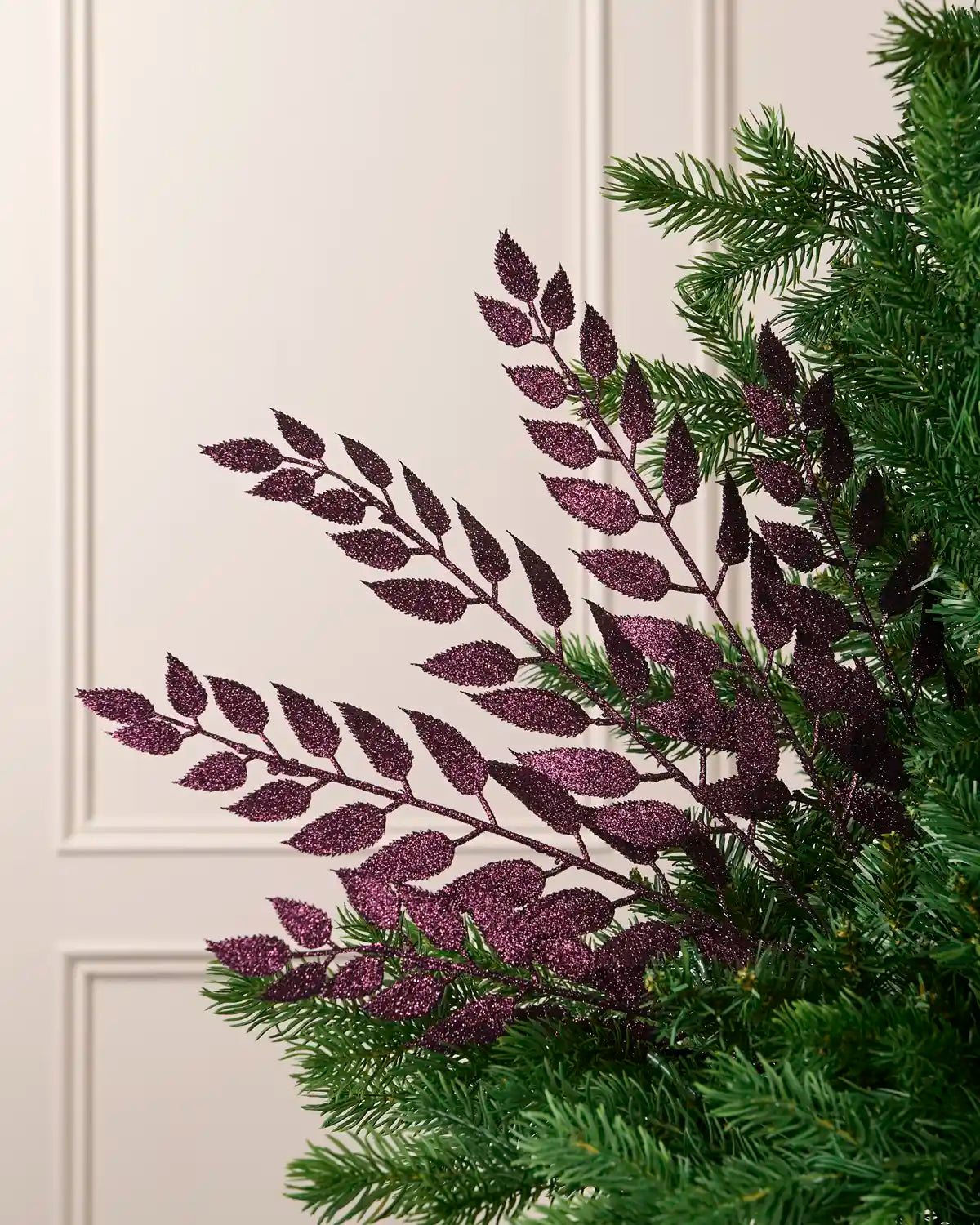 Purple leaf Christmas tree spray arranged among green Christmas tree branches.