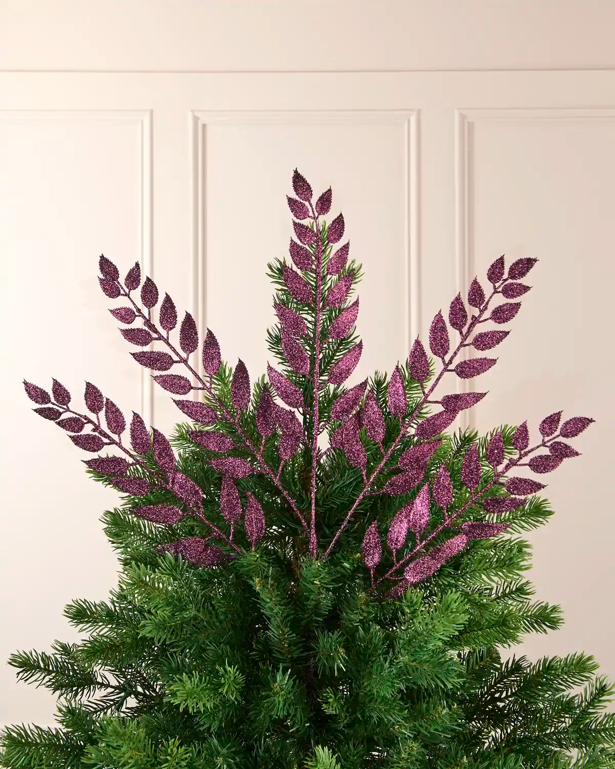Purple leaf Christmas tree spray styled at the top of a green Christmas tree.