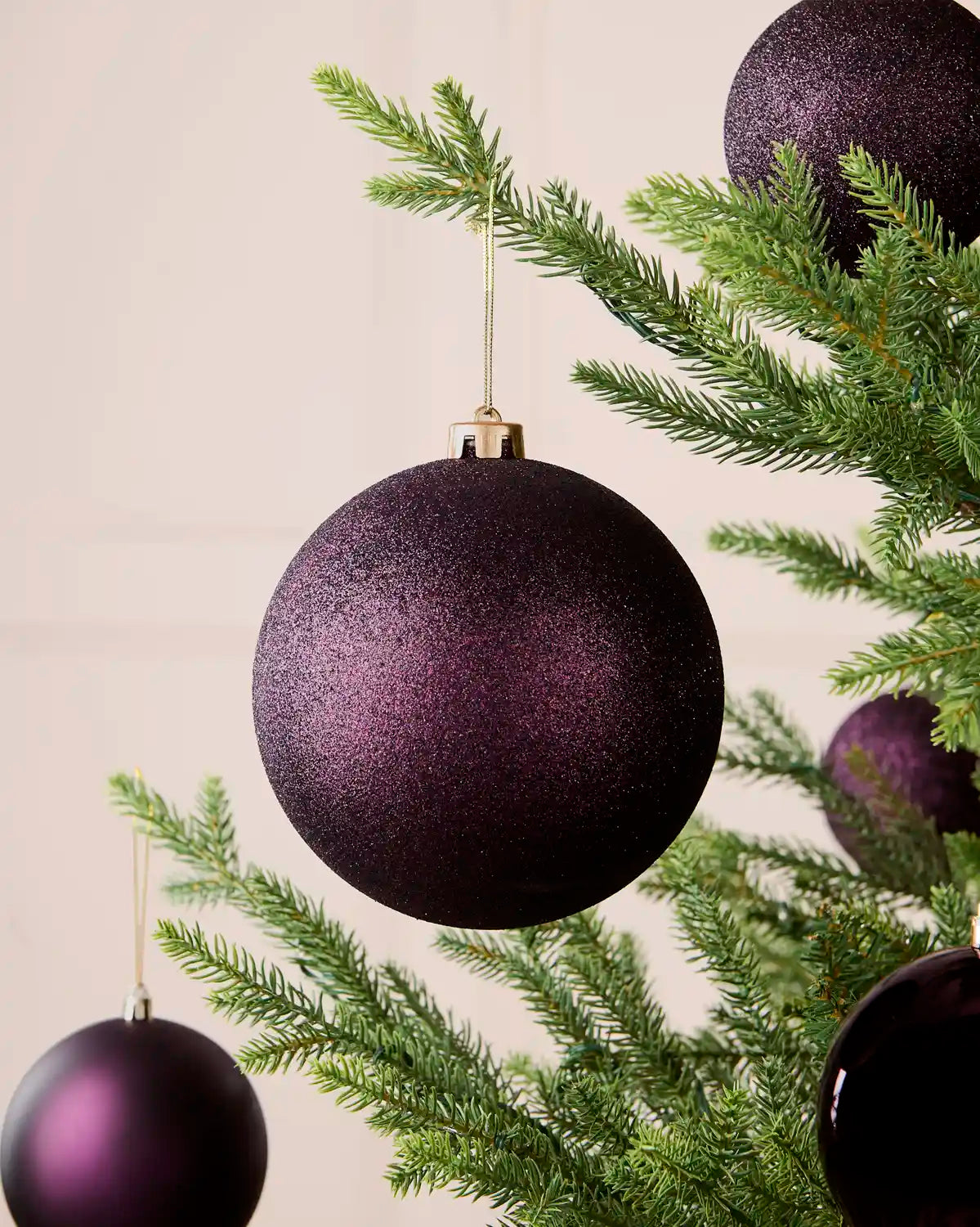 Oversized 15 cm purple glitter shatterproof bauble displayed on a Christmas tree with coordinating purple baubles.