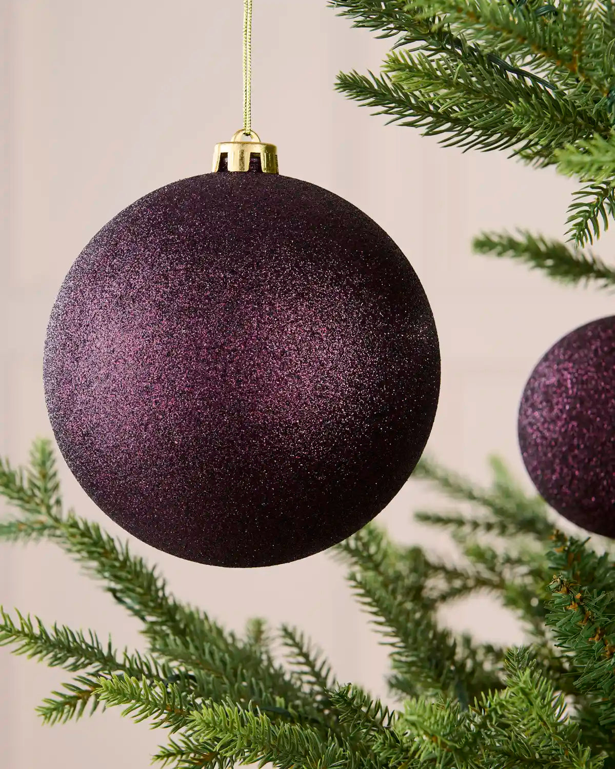 Close-up of a 15 cm oversized purple shatterproof bauble with a sparkling glitter finish on a Christmas tree.