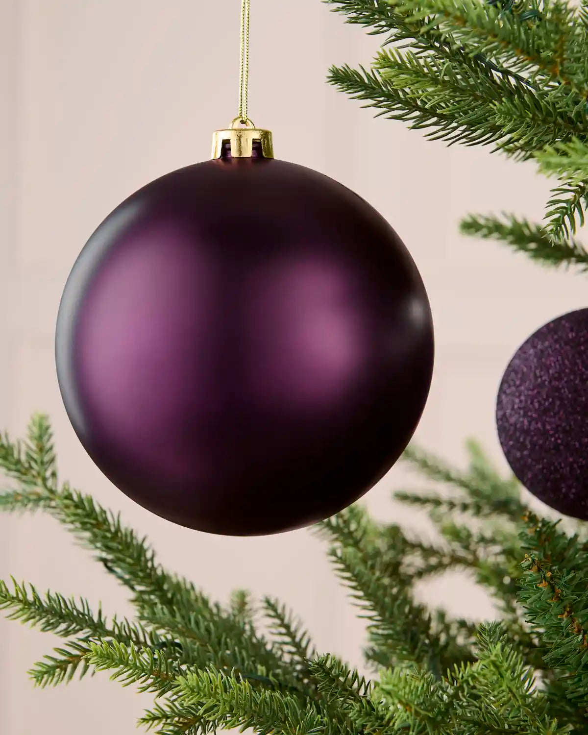 Close-up of a 15 cm oversized purple shatterproof bauble with a smooth matt finish hanging on a Christmas tree.