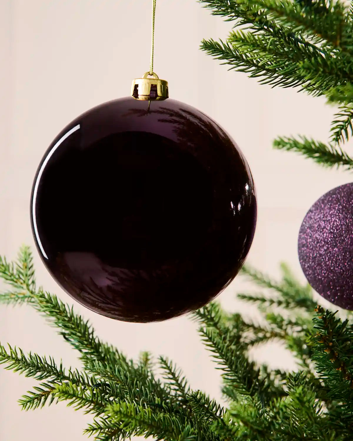 Close-up of a 15 cm oversized purple shatterproof bauble with a shiny finish hanging on a Christmas tree.
