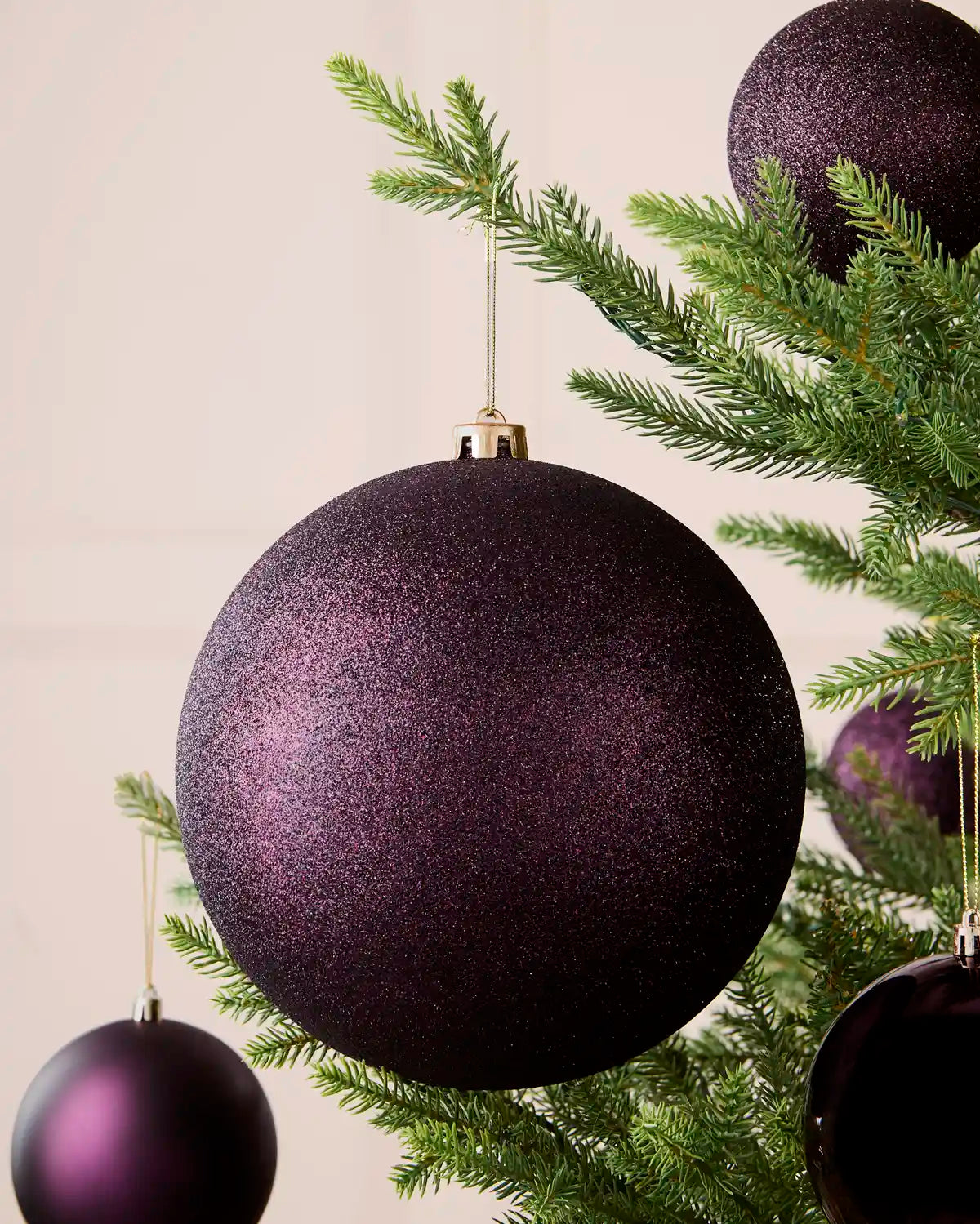 Oversized 20 cm purple glitter shatterproof bauble displayed on a Christmas tree with coordinating purple baubles.