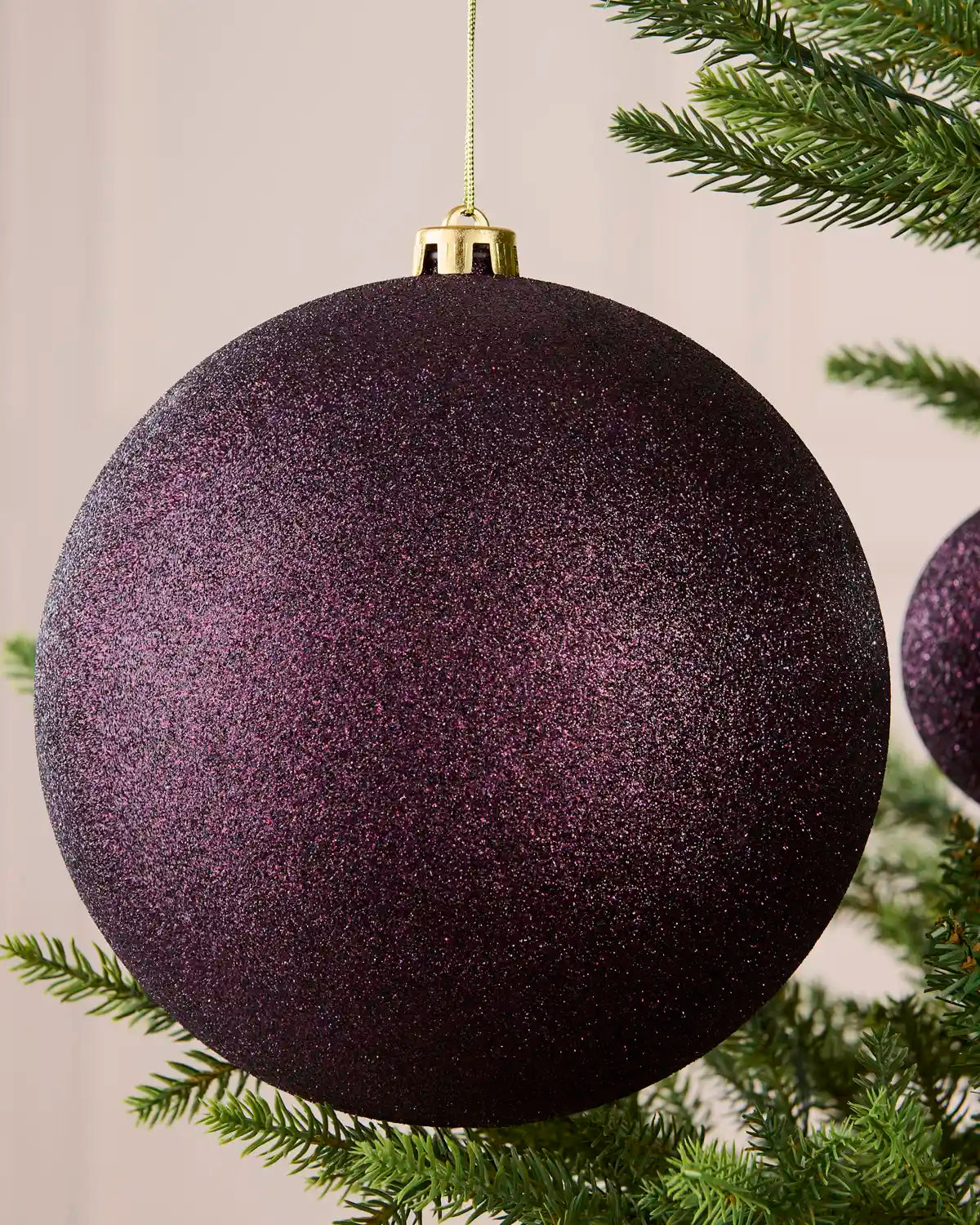 Close-up of a 20 cm oversized purple shatterproof bauble with a sparkling glitter finish on a Christmas tree.