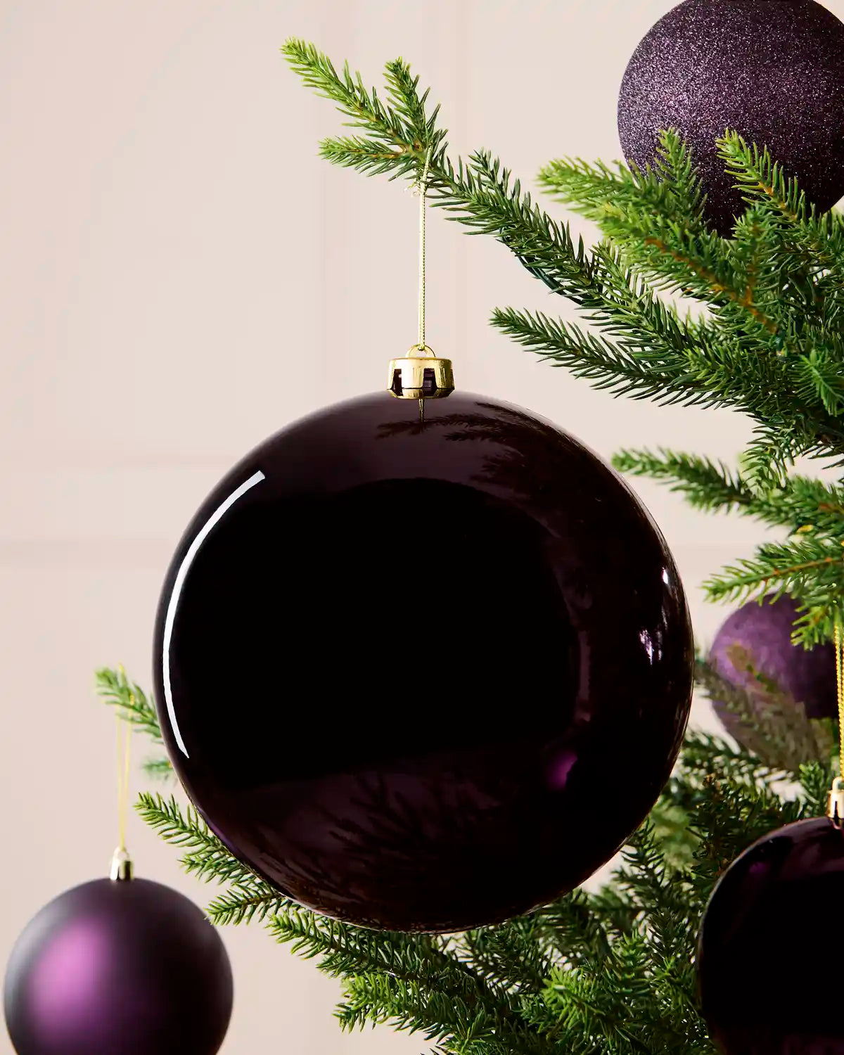 Oversized 20 cm purple shiny shatterproof bauble displayed on a Christmas tree with coordinating purple baubles.