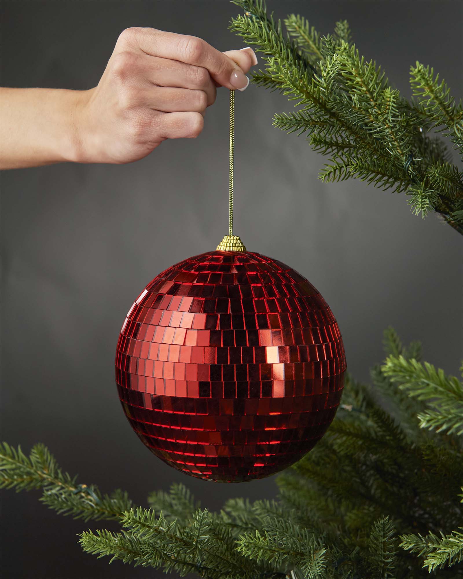 Hand holding a red 15cm oversized disco ball bauble beside a Christmas tree.