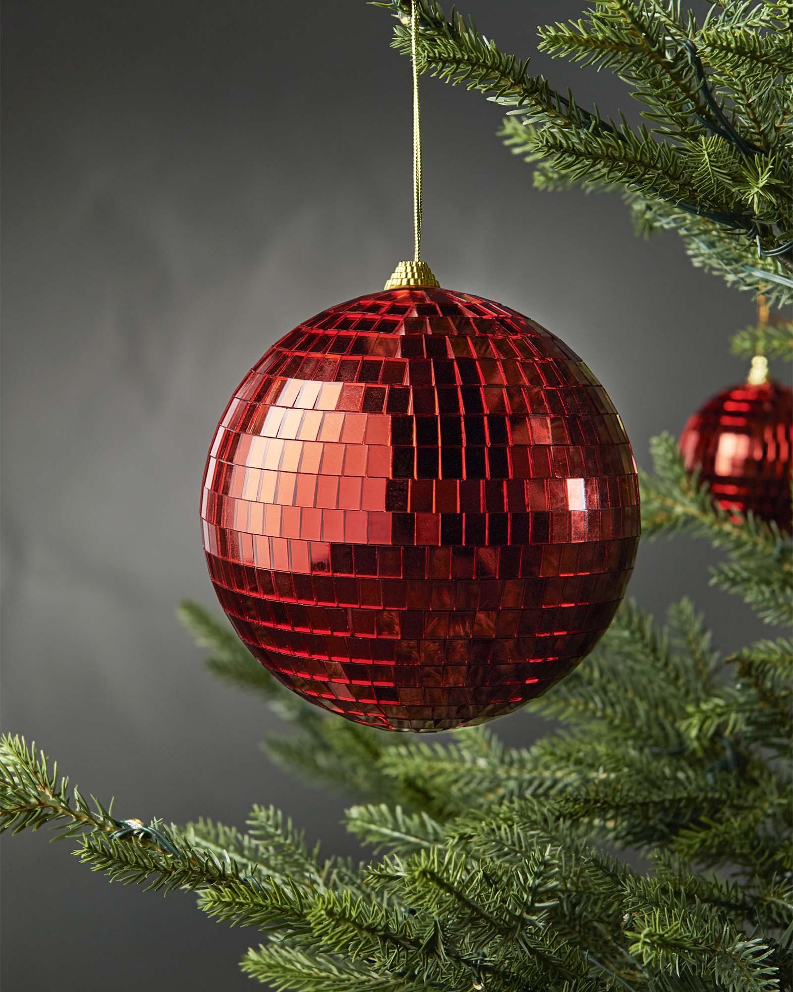 Red 15cm oversized disco ball bauble hanging on a Christmas tree.