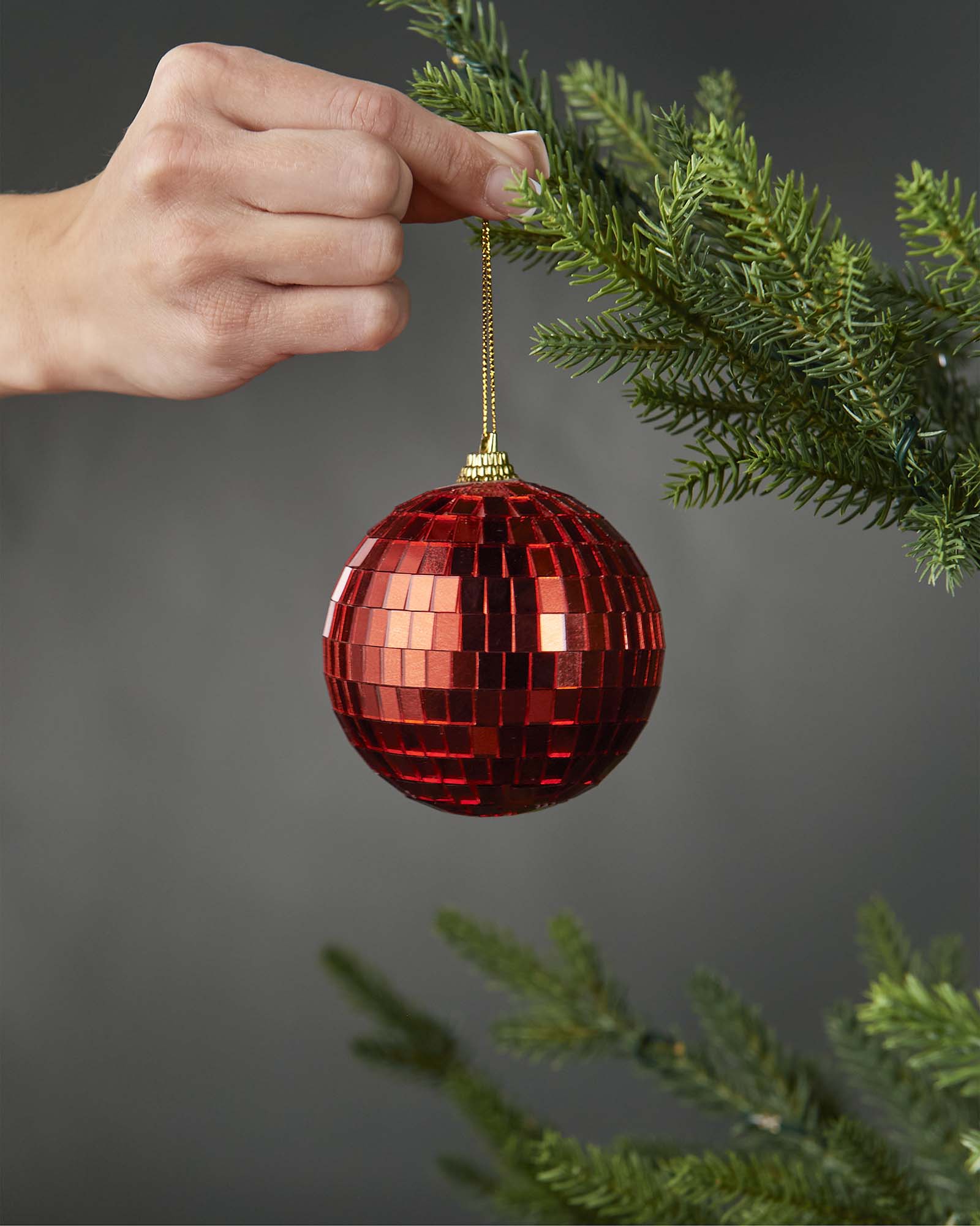 Hand holding a red 8cm disco ball bauble beside a Christmas tree.