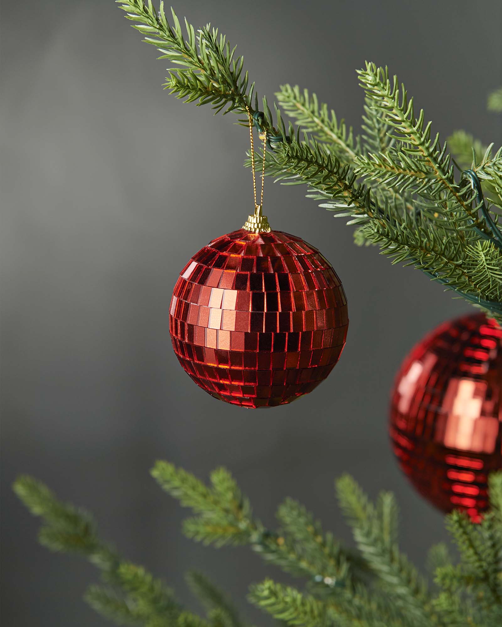 Red 8cm disco ball bauble hanging on a Christmas tree branch.