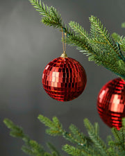 Red 8cm disco ball bauble hanging on a Christmas tree branch.