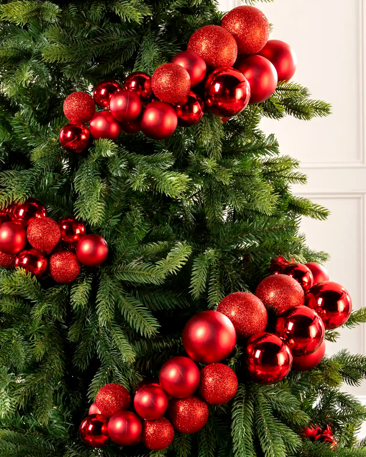 Close-up of red bauble cluster arch on a Christmas tree showing mixed sizes and finishes.