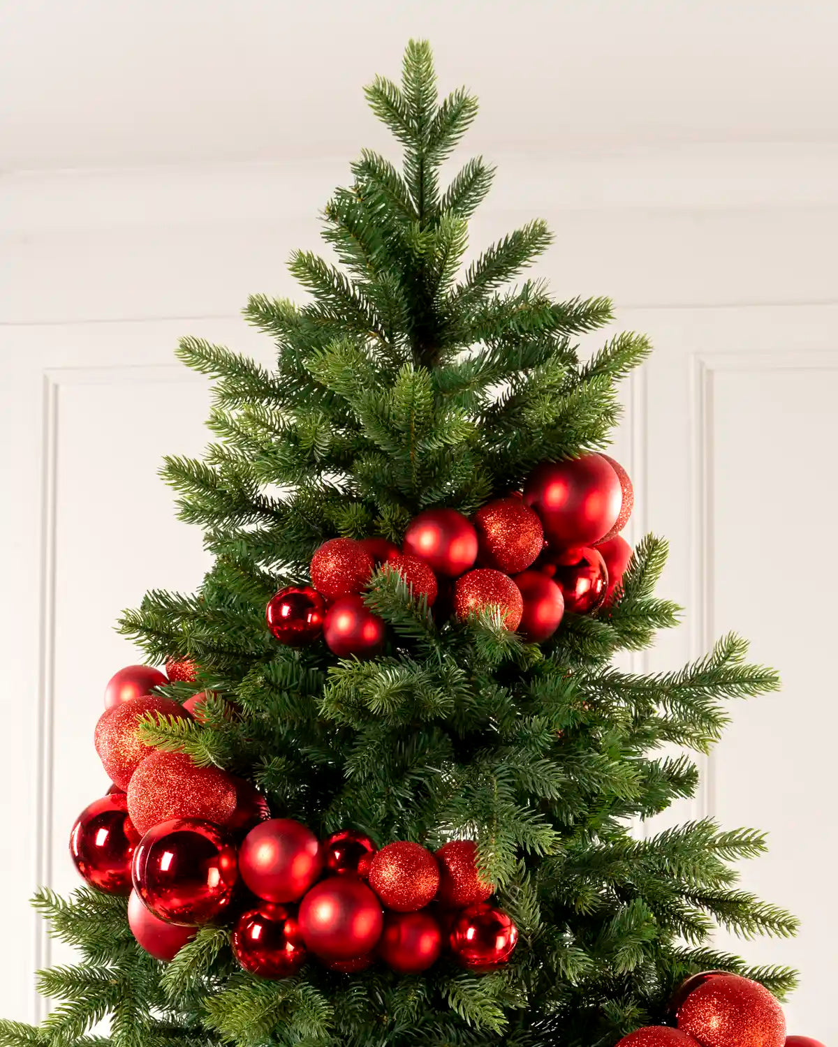 Red bauble cluster arch arranged through the upper branches of a green Christmas tree.
