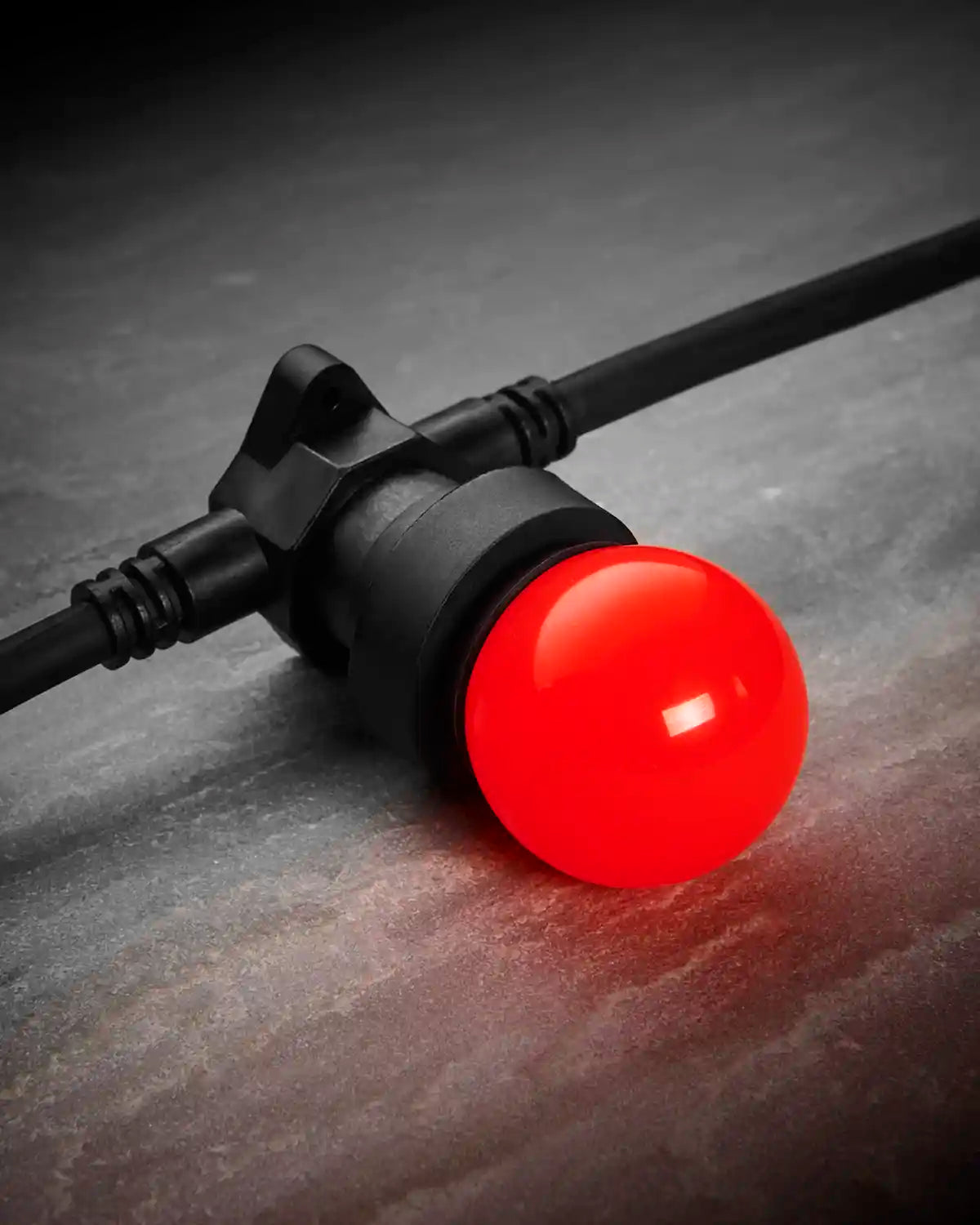 Close-up of a red E27 LED bulb fitted into a black festoon belt on a dark stone-effect surface.