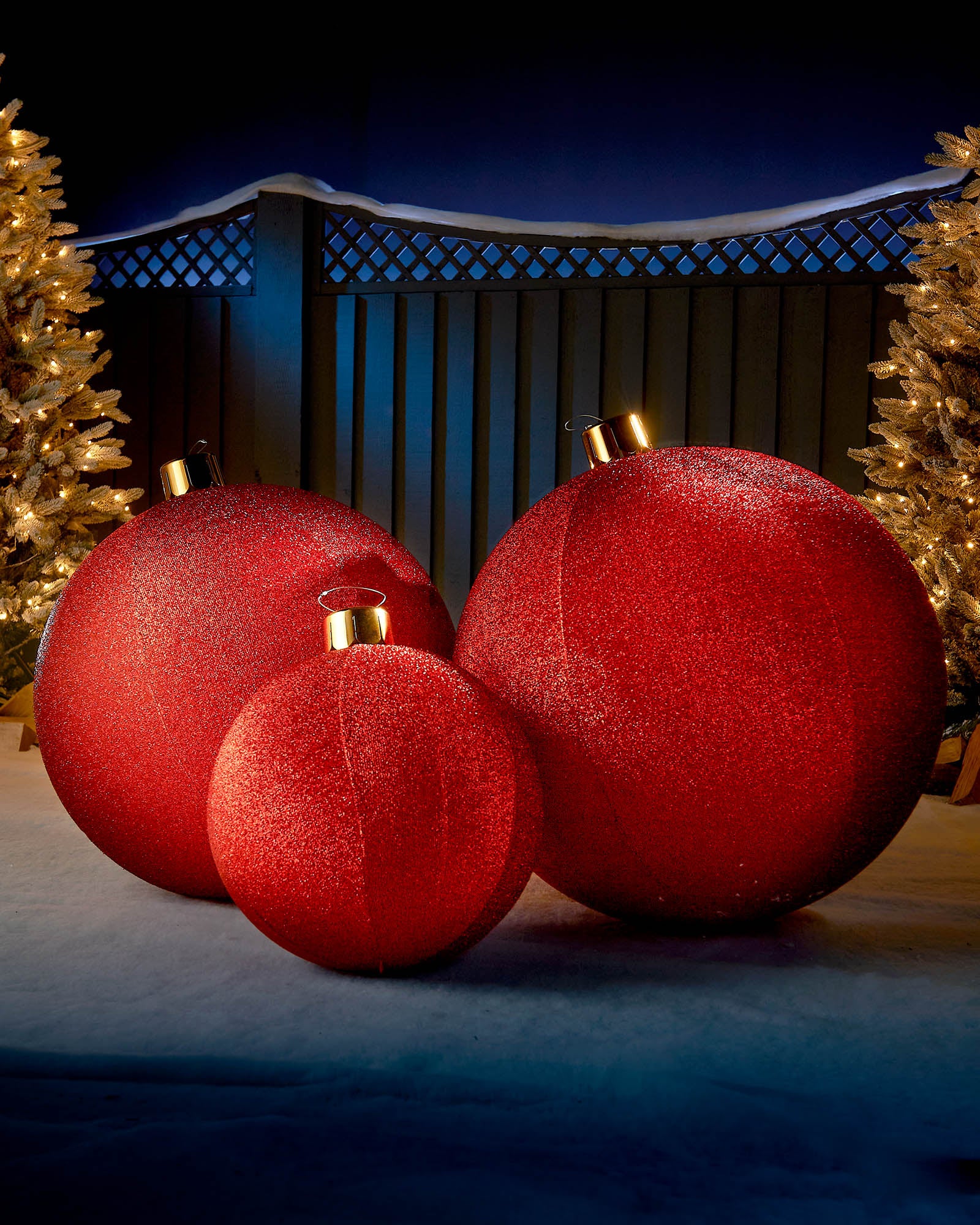 Red inflatable tinsel Christmas baubles in different sizes displayed outdoors with warm festive lights.