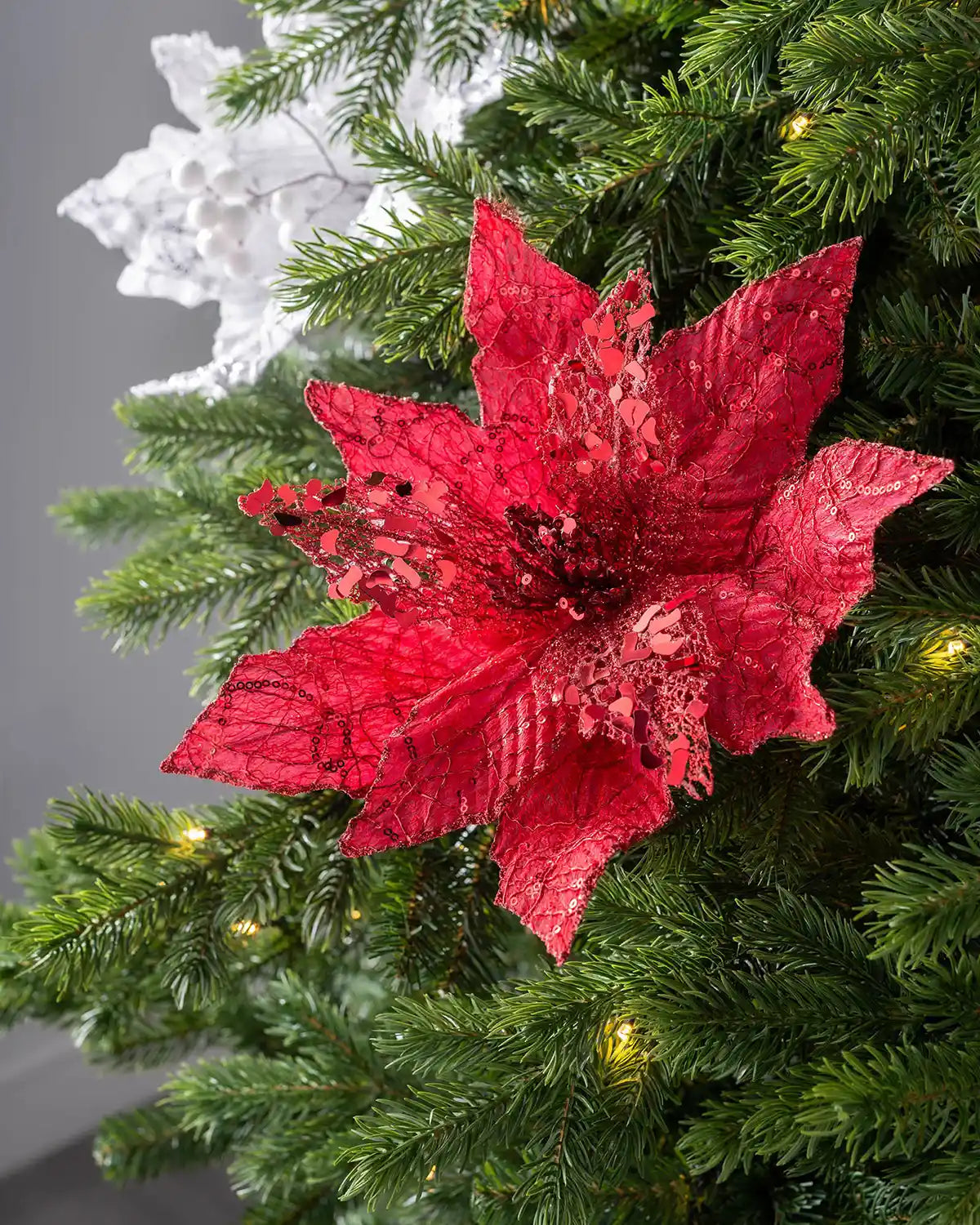 Red artificial poinsettia flower with sequin and glitter detail in a tree