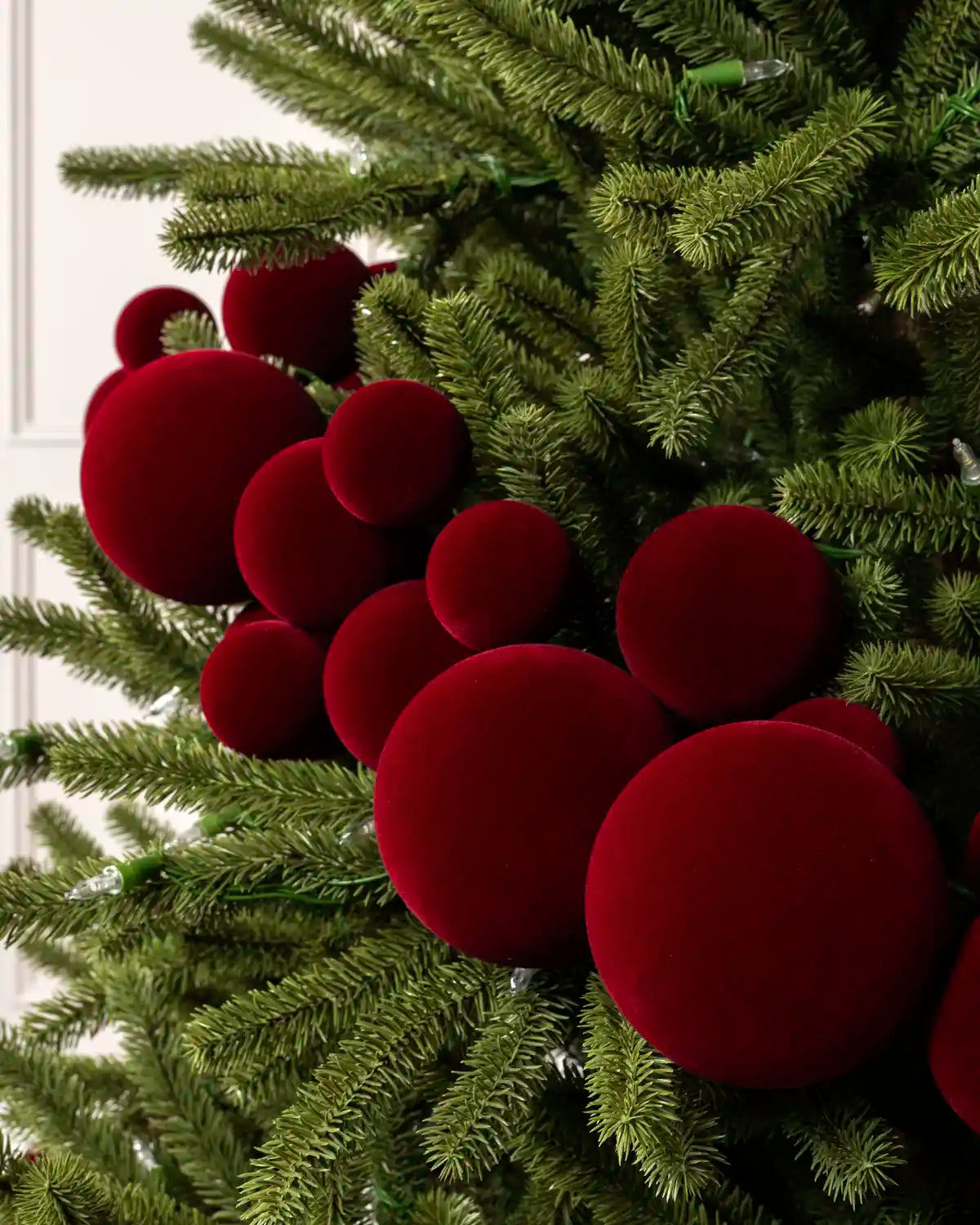 Close-up of red velvet bauble garland on a Christmas tree showing the soft textured finish and mixed bauble sizes.