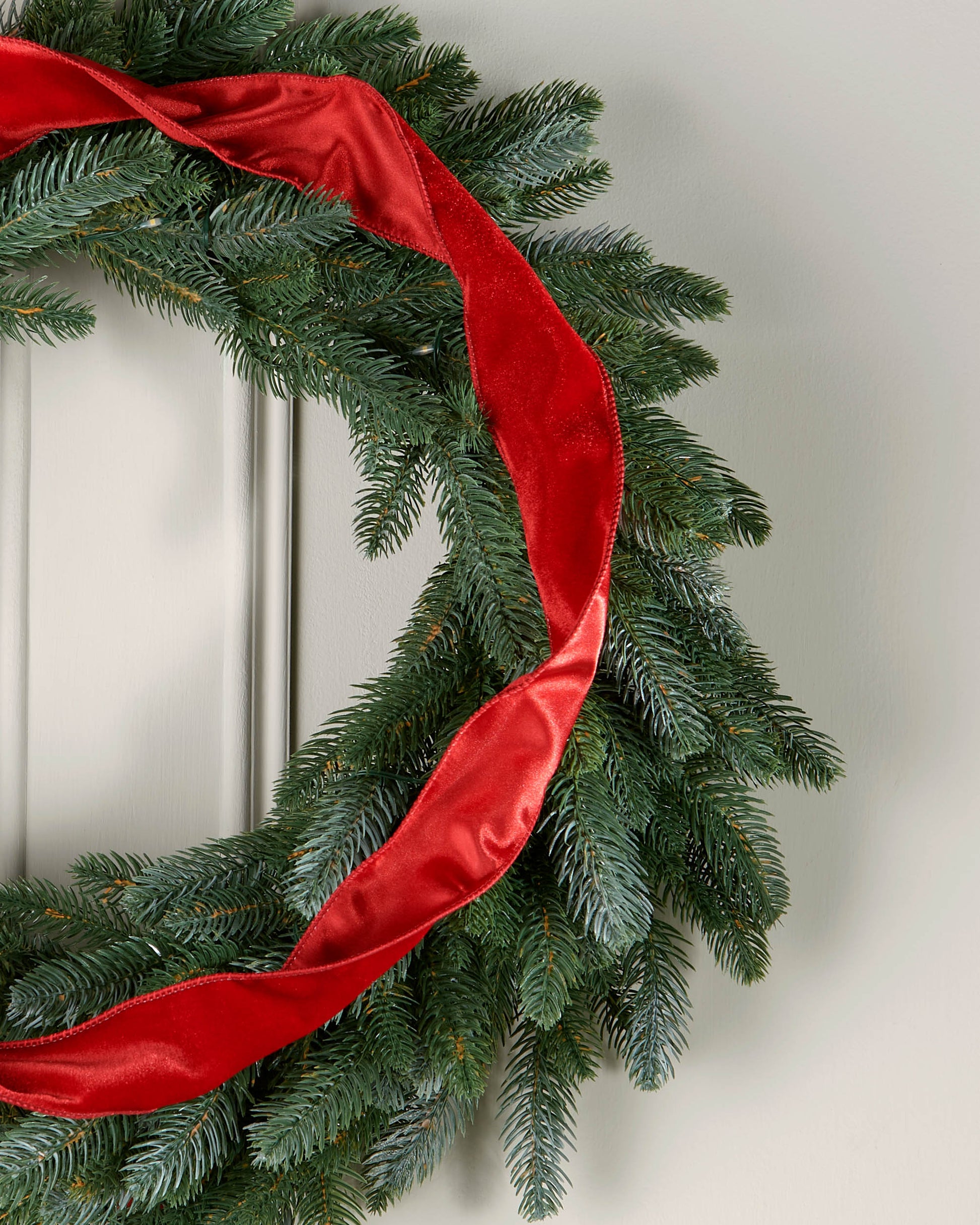 Red velvet ribbon styled in a loose spiral on a green Christmas wreath.