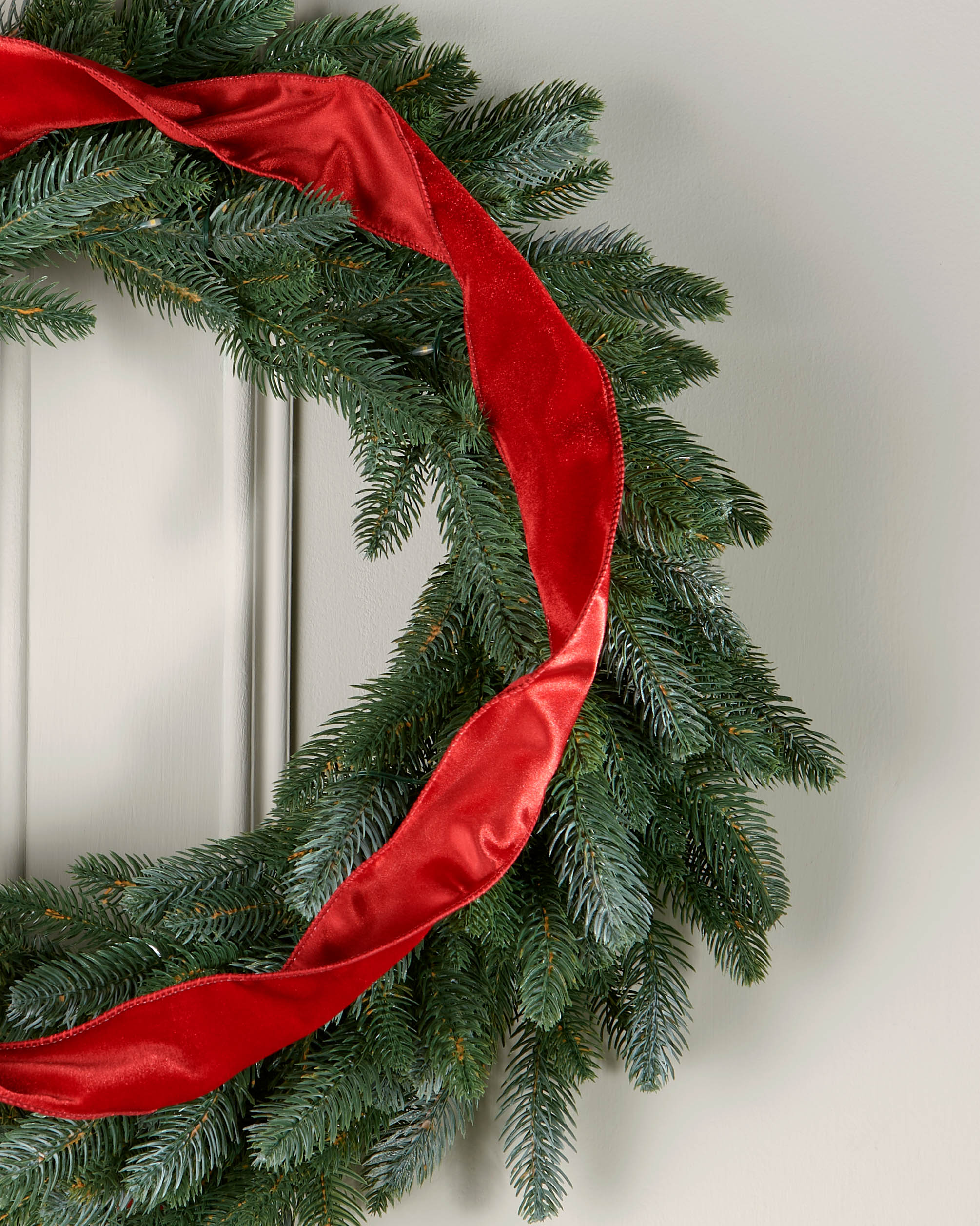 Red velvet ribbon styled in a loose spiral on a green Christmas wreath.