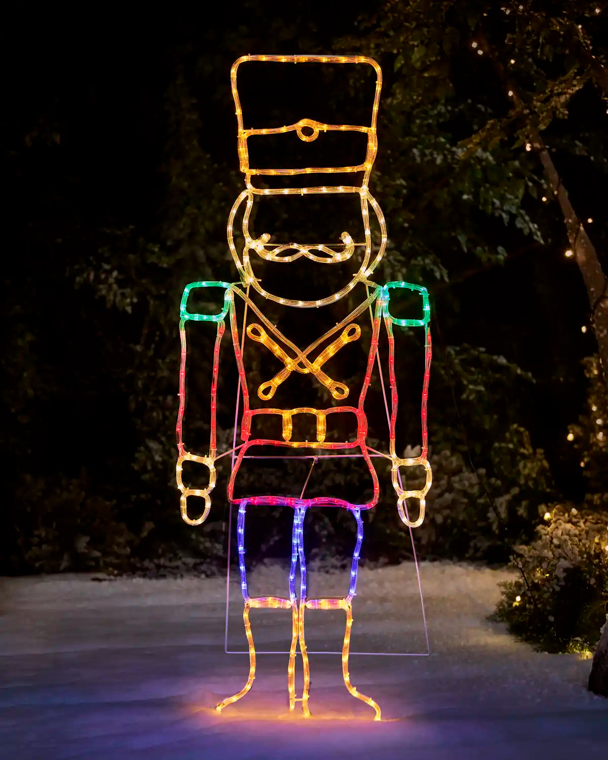 red, blue, green and warm white  Nutcracker rope light silhouette on snowy grass against a dark garden setting 